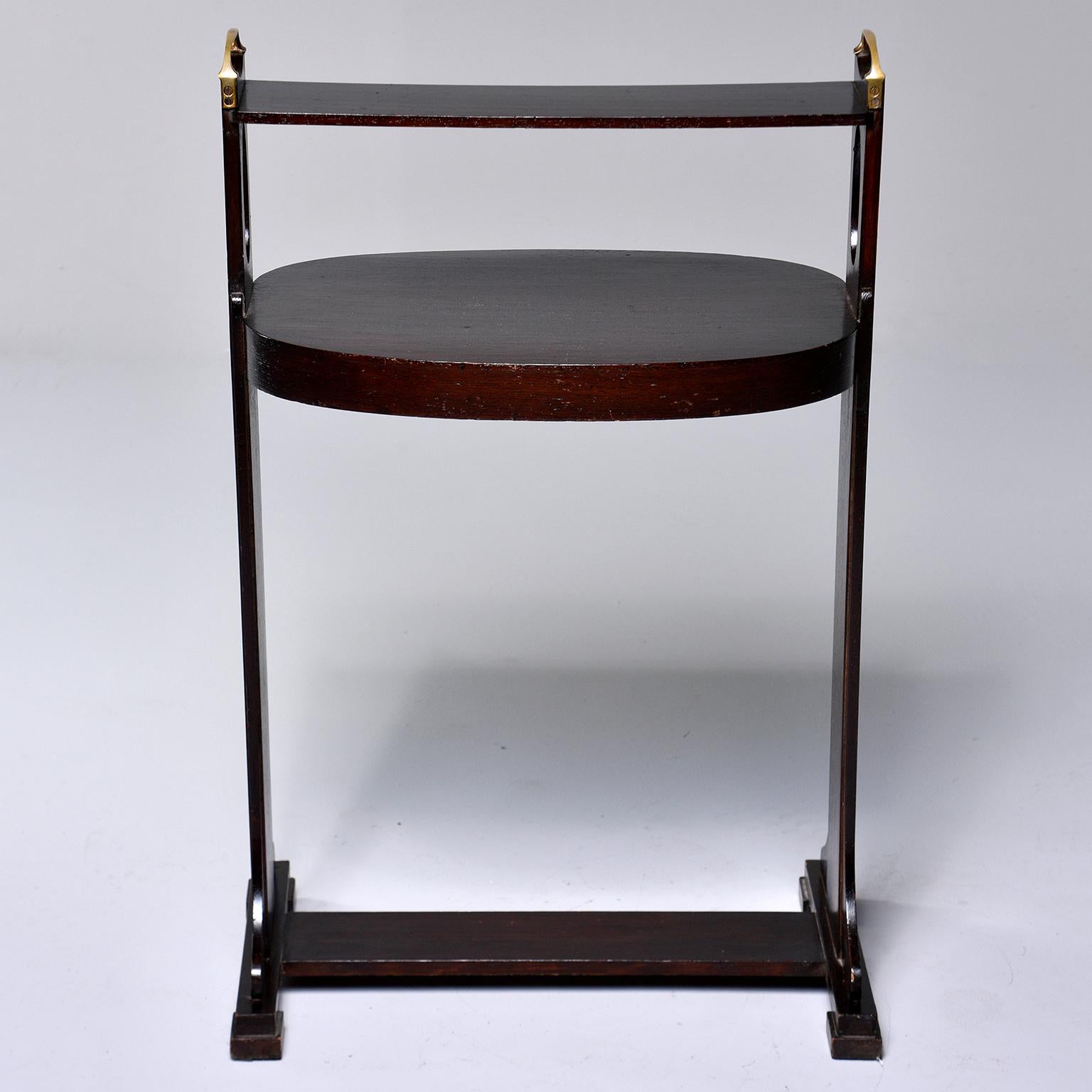 Arts & Crafts dark stained palisander stand or side table, circa 1920s. Footed base with decorative cutout in side supports, oval tabletop and narrow top rail with brass handles. Unknown maker. Found in England.