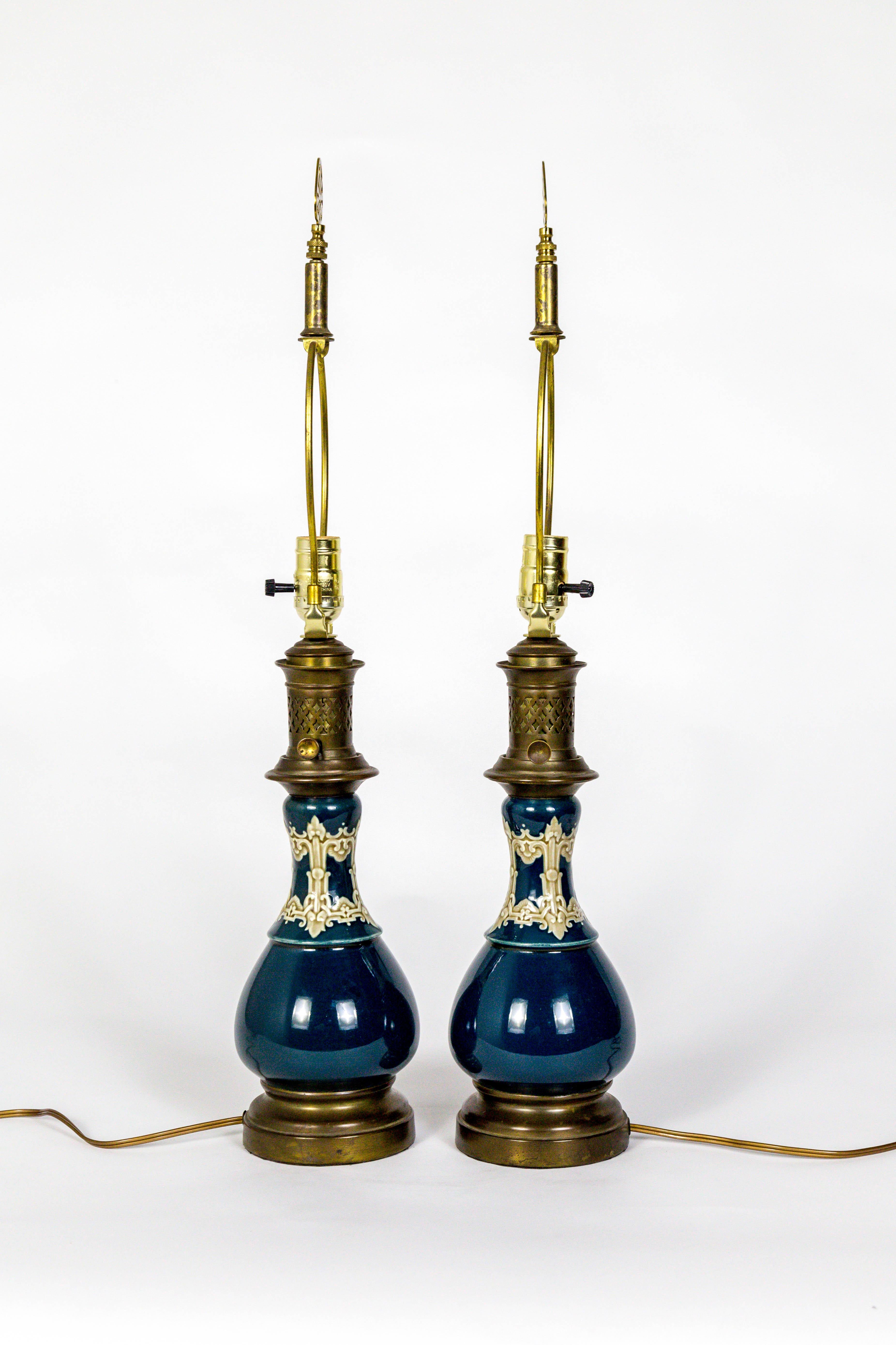 A lovely pair of ceramic, late 19th century, converted kerosene lamps in dark turquoise with modeled details in muddy green and cream. Wonderful brass piecework chimneys and keys, with complimenting brass finials. Dutch, 1880s. Measures: 27