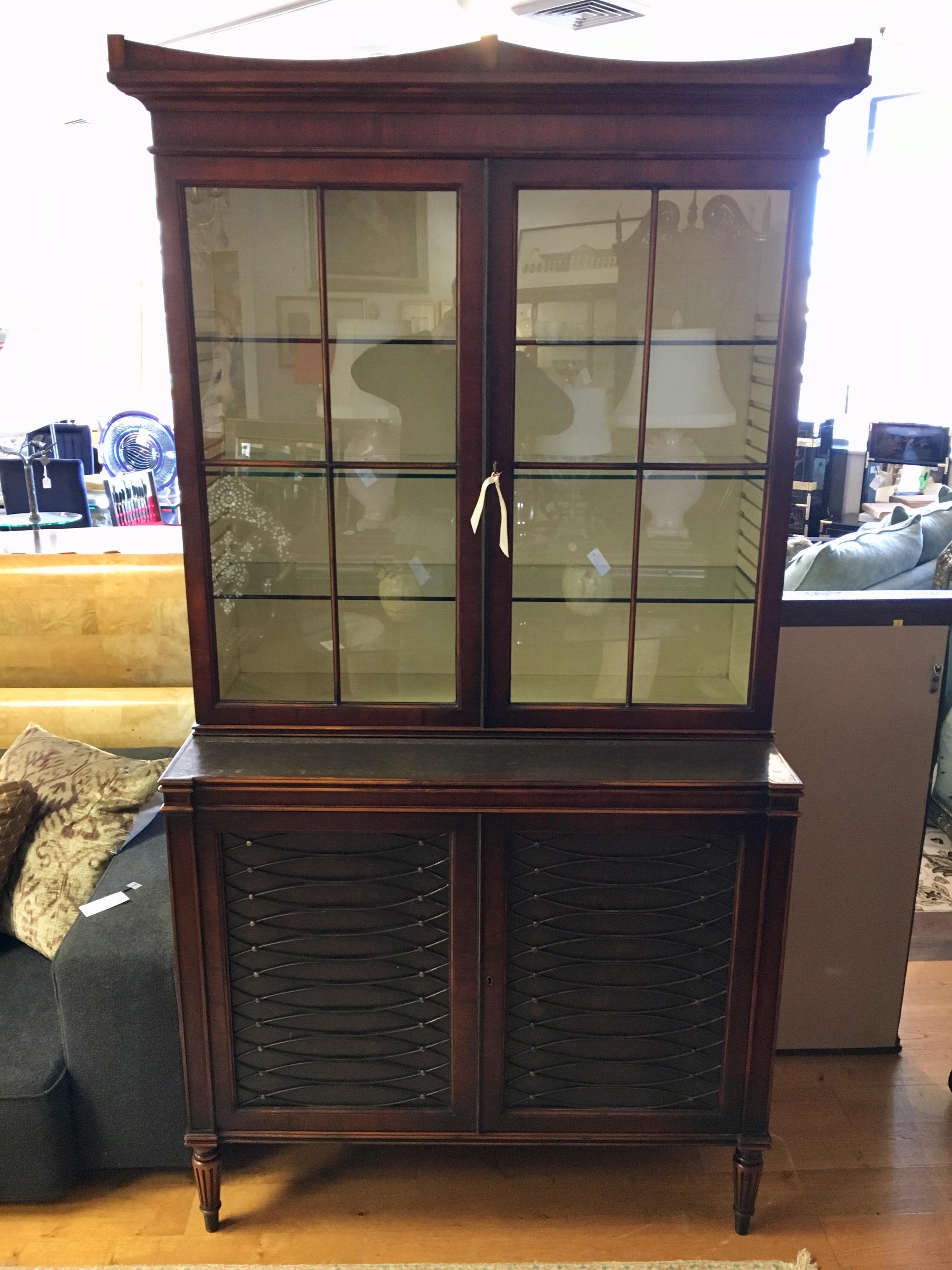 Stunning dark walnut and leather breakfront from Rinfret, Greenwich, CT. It is illuminated and features
lockable storage at top and bottom. Top has three shelves and bottom has one wooden shelf. Comes in two pieces, top and bottom, for ease of