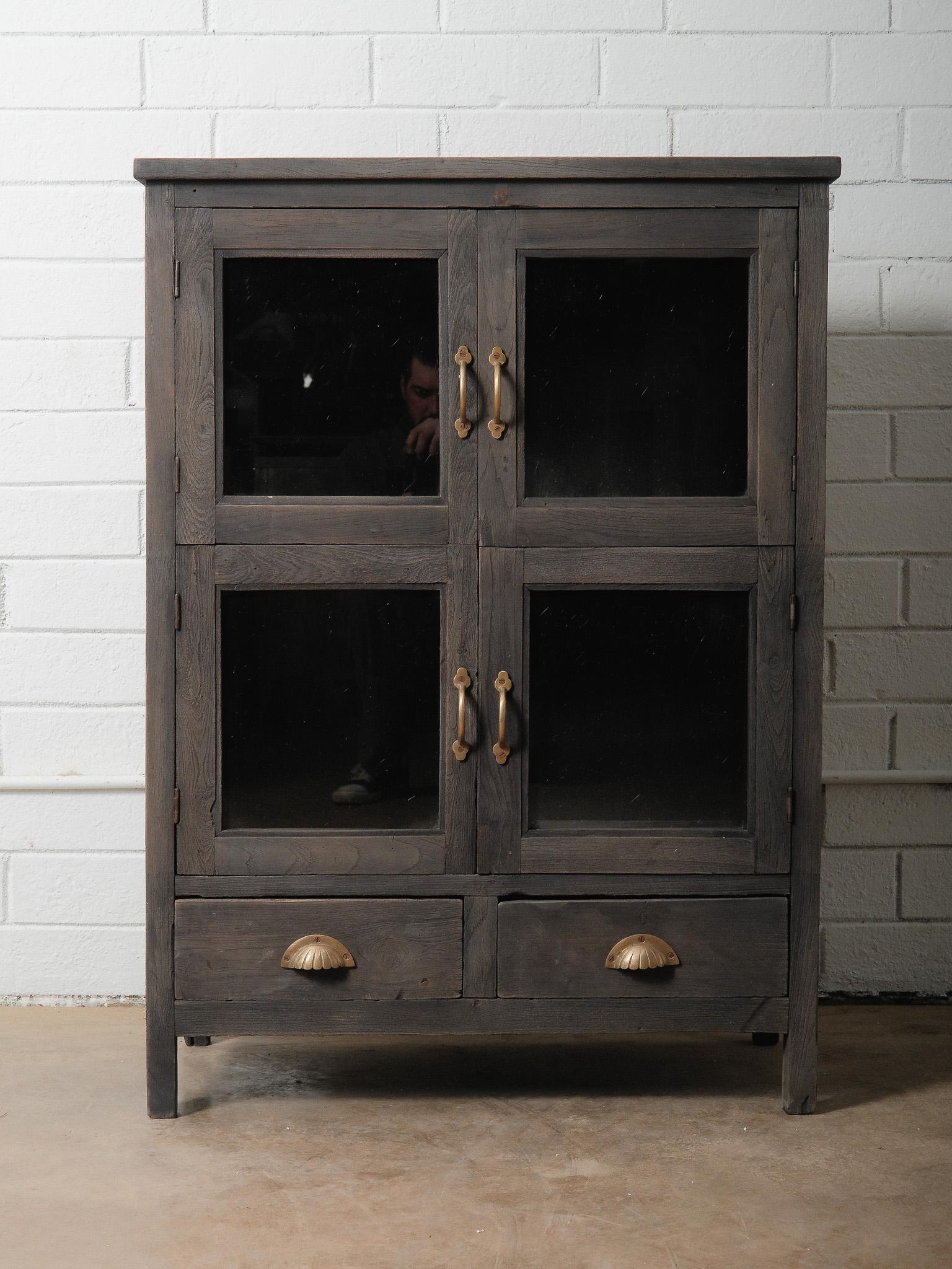 Cette armoire vintage en bois foncé à façade vitrée offre un mélange intemporel de charme rustique et de rangement fonctionnel. Fabriquée avec des lignes simples et terreuses et une finition naturellement vieillie, la pièce comporte quatre portes en