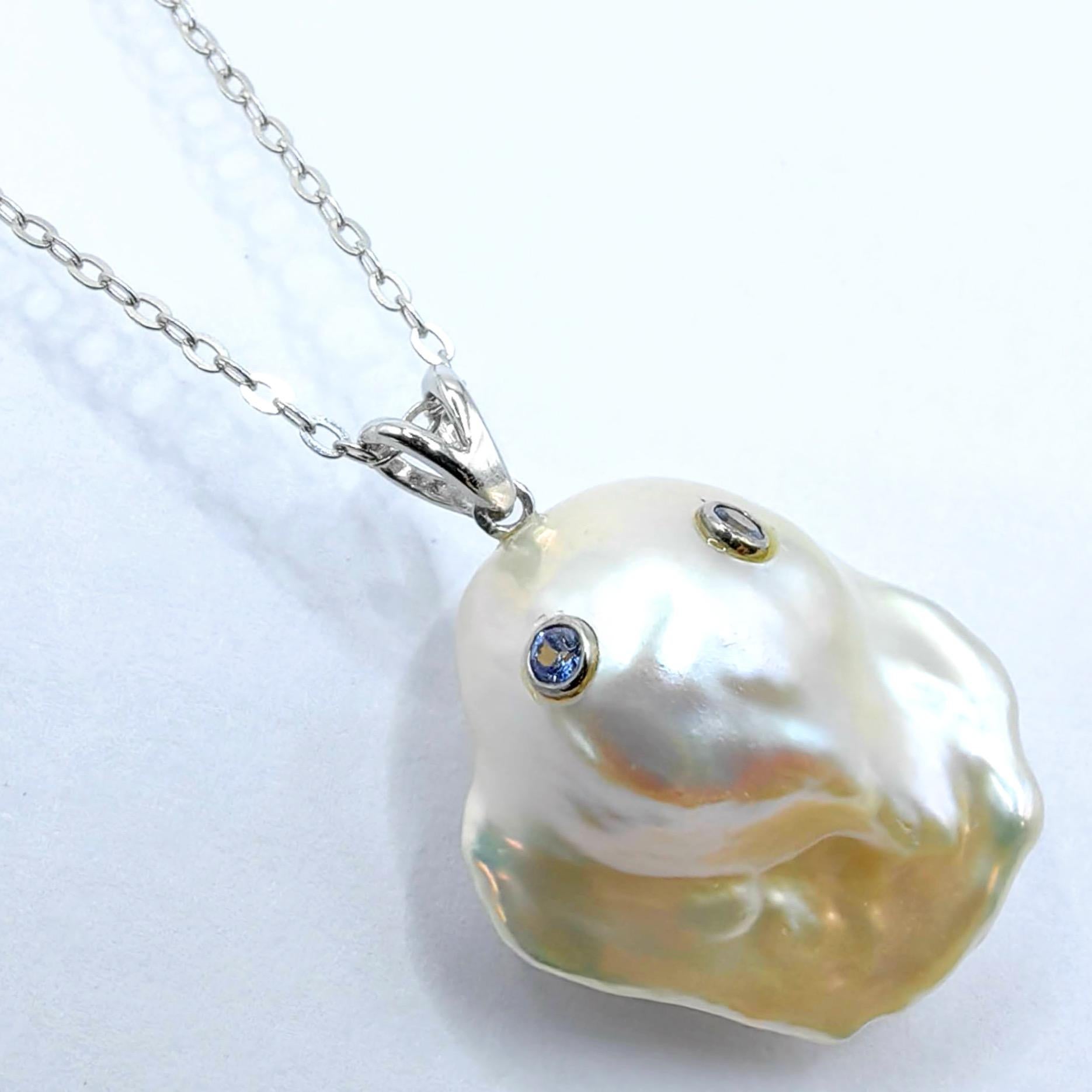 Scopri l'incantevole Darling Phantom: ciondolo fantasma in oro bianco 18 carati con zaffiro azzurro e perla barocca, che evoca lo spirito di un fantasma gentile ed etereo. Questa perla barocca bianca d'acqua dolce, del peso di 21,40 carati, è una