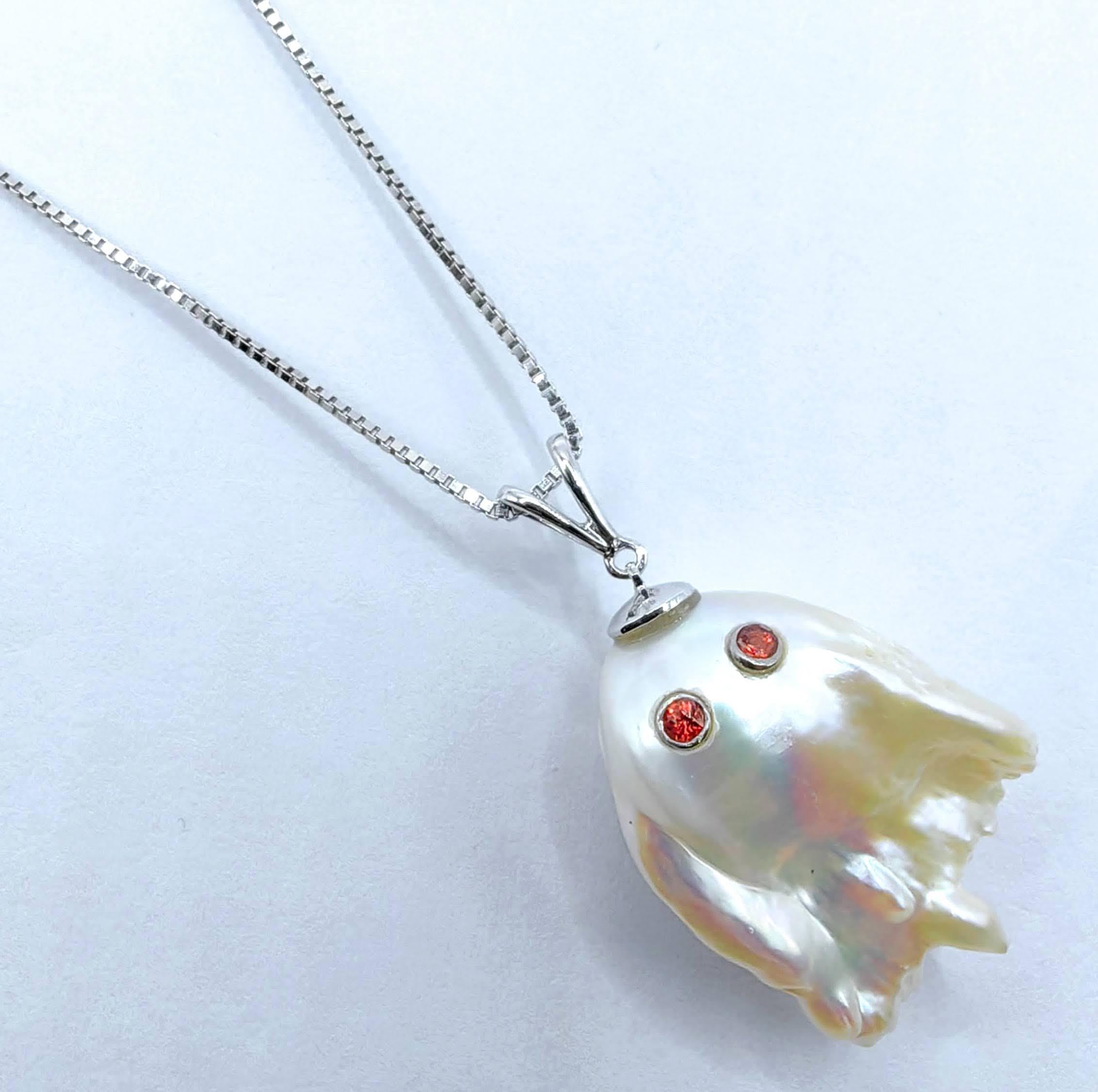 Enthüllen Sie den bezaubernden Anhänger Darling Phantom: Orange Sapphire Baroque Pearl Ghost aus 18 Karat Weißgold, der den Geist eines schelmischen und doch charmanten Gespenstes heraufbeschwört. Dieser bezaubernde Anhänger mit einer Länge von ca.
