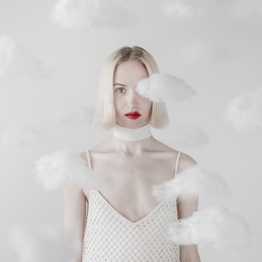 This beautifully vibrant portrait of a woman with red lipstick that is purposefully off-kilter combines surreal elements of clouds floating in the space.  
This is a limited edition color photograph. Number 1 of 5 is currently available, framed in