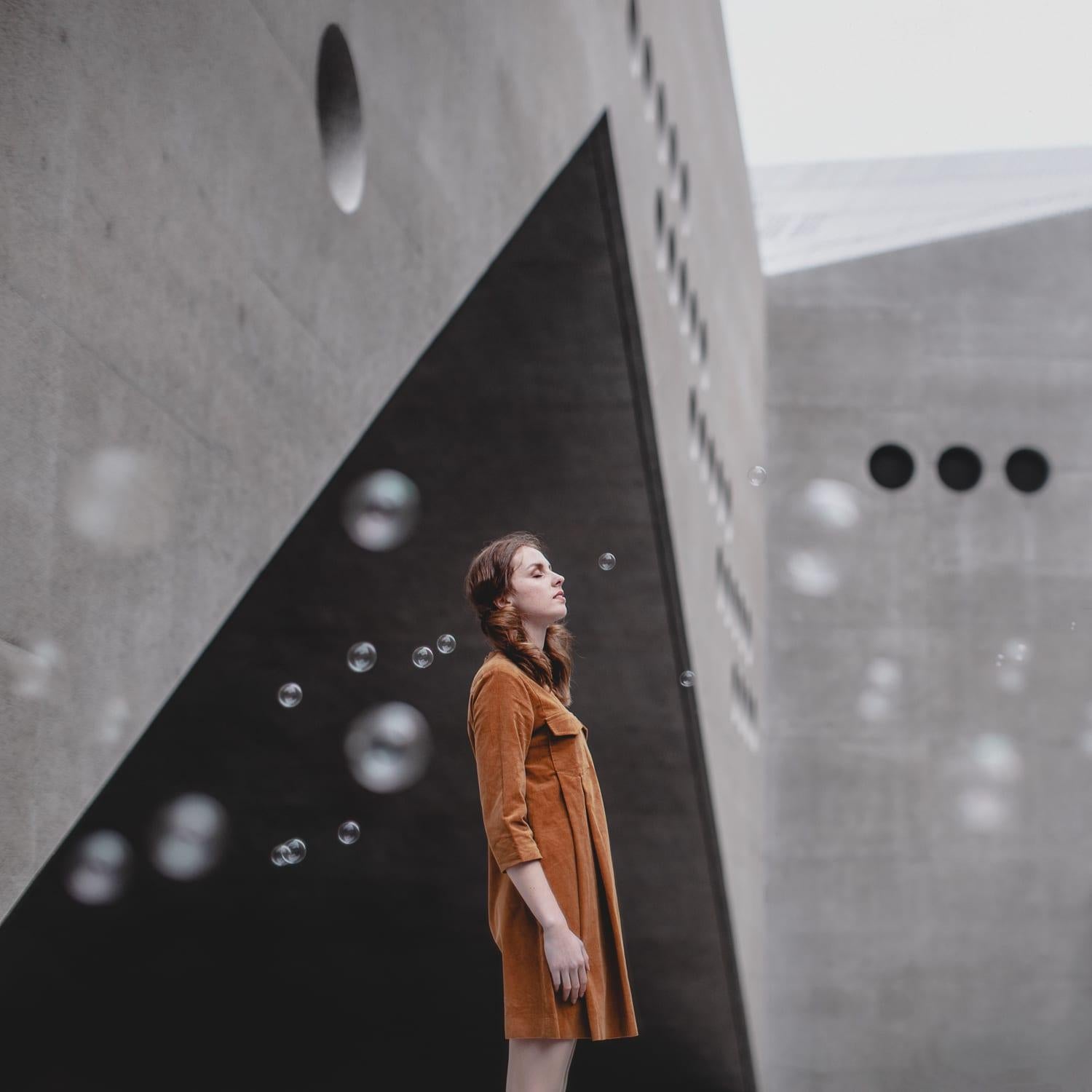 Photographie couleur encadrée avec femme, bulles, architecture géométrique grise, orange