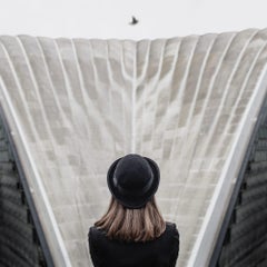 Gerahmte Farbfotografie einer Frau mit schwarzem Hut im Magritte-Stil, graue Architektur