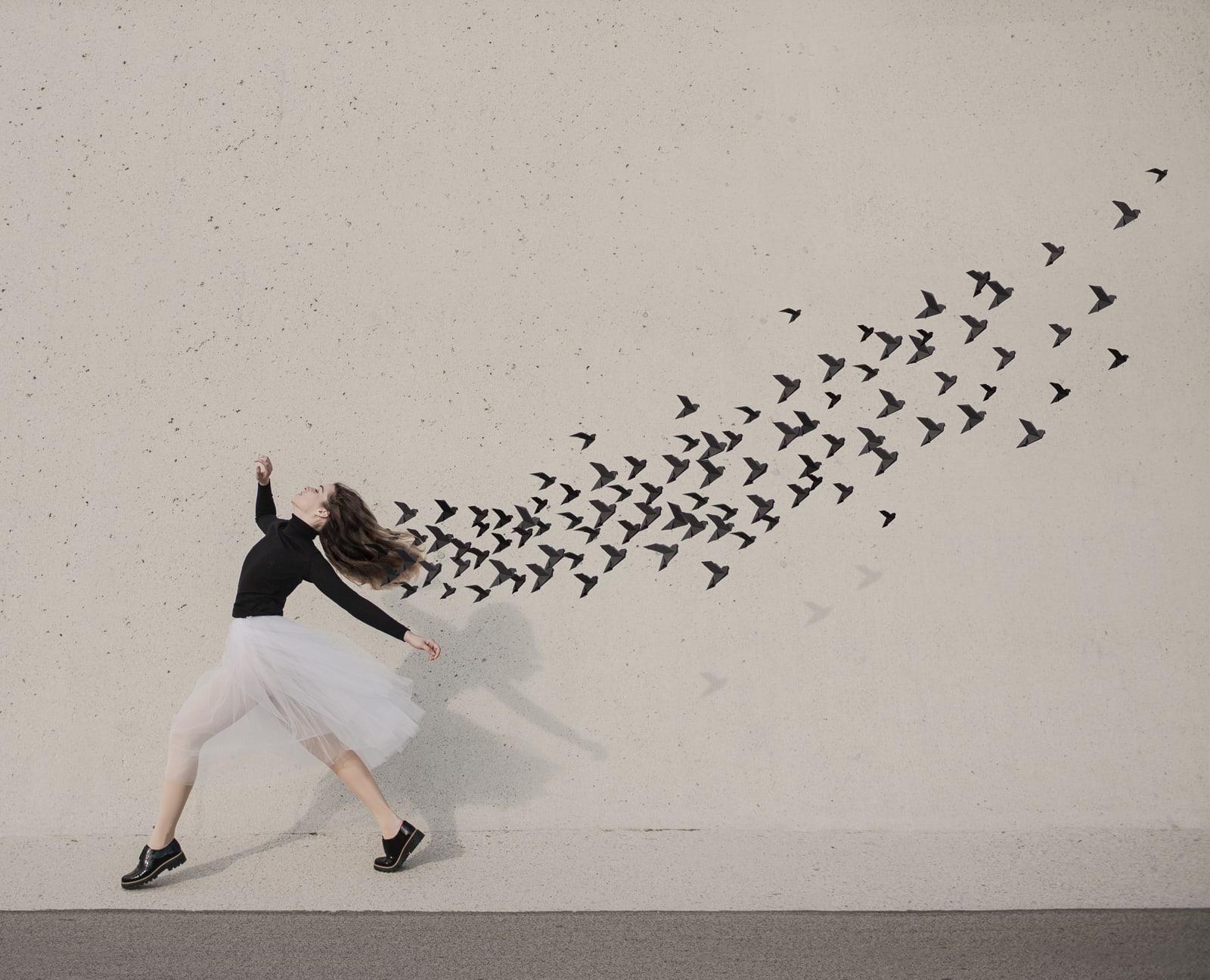 This surrealist portrait uses a minimalist palette of mostly black and white. The model is in mid flight as she dances through life. Hand-made origami birds trail behind her. This color photograph was shot in Vienna. This is a limited edition
