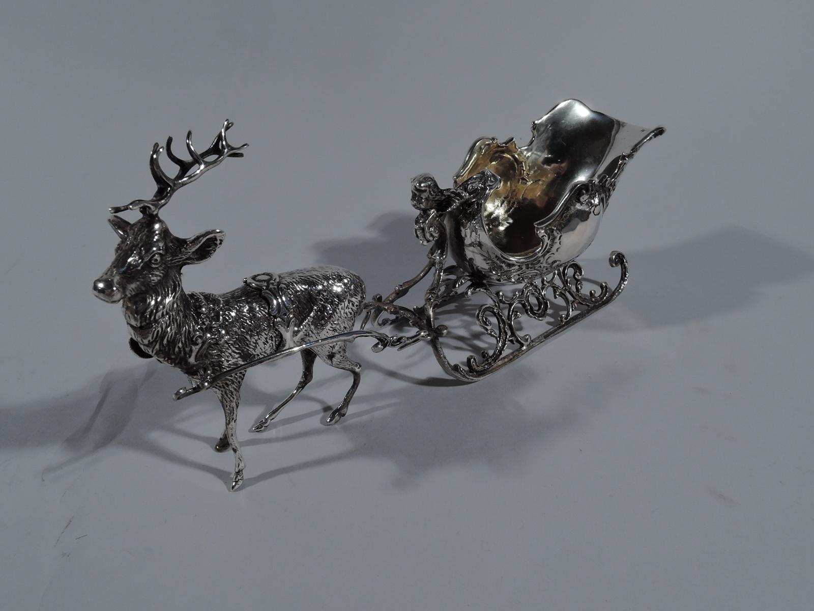 Turn-of-the-century German 800 silver sleigh. Shaped ovoid body with chased scrolls and flowers mounted to ornamental runners harnessed to bristly-furred and flamboyantly-horned reindeer. A fantasy vehicle that seats one. Get away from bad vibes and