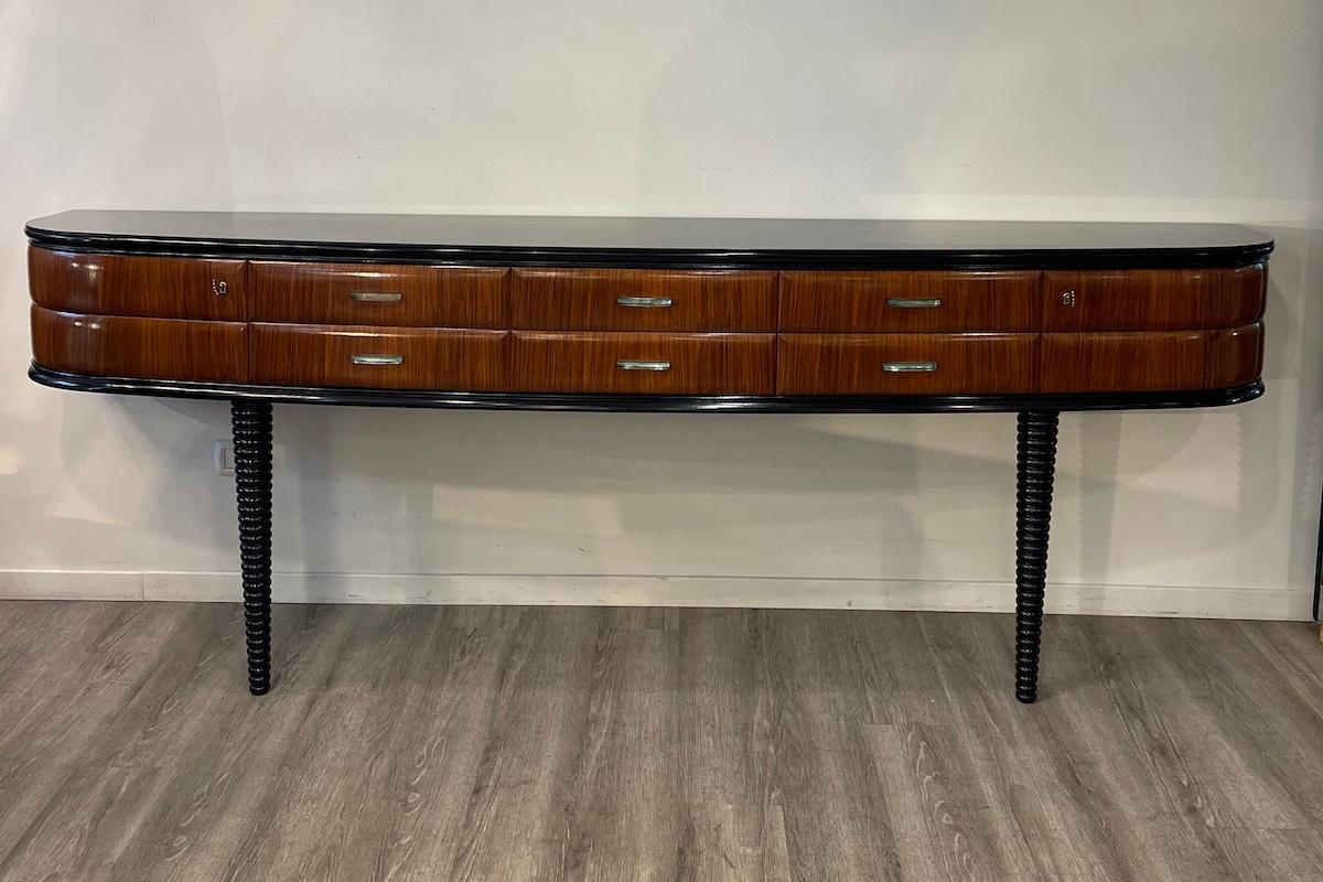 Console in legno degli anni '50. Ciò che rende unica questa consolle è il suo design, caratterizzato da due sole gambe ritorte che sostengono il pezzo e che le conferiscono un aspetto più leggero. 
La console è stata disegnata da Dassi, con maniglie