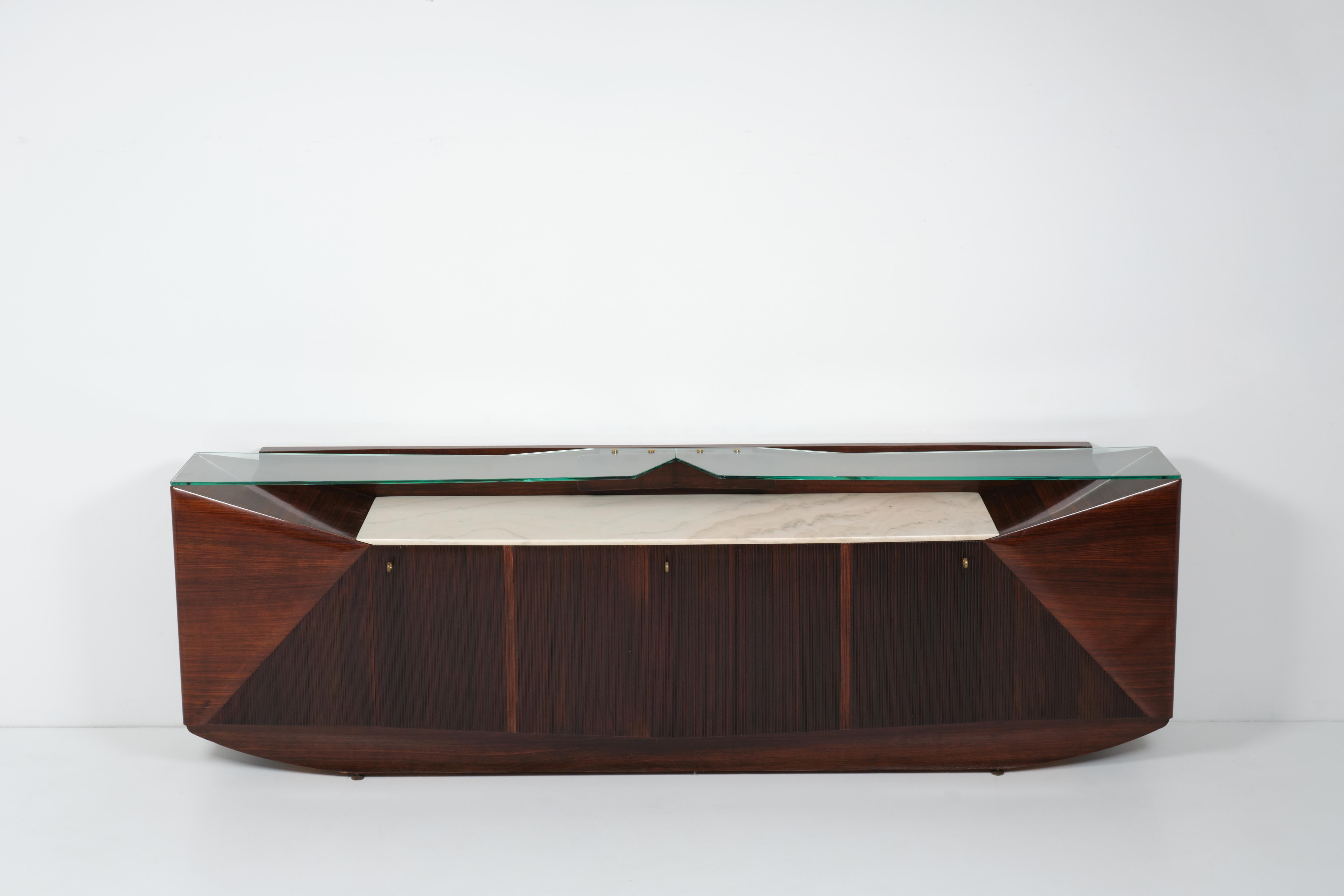 This big sideboard was manufactured by Dassi in the '50s. Its walnut body is embellished by tops mounted on different levels respectively in marble and bevelled glass, while brass details finish this solid yet elegant item.
Equipped with shelves