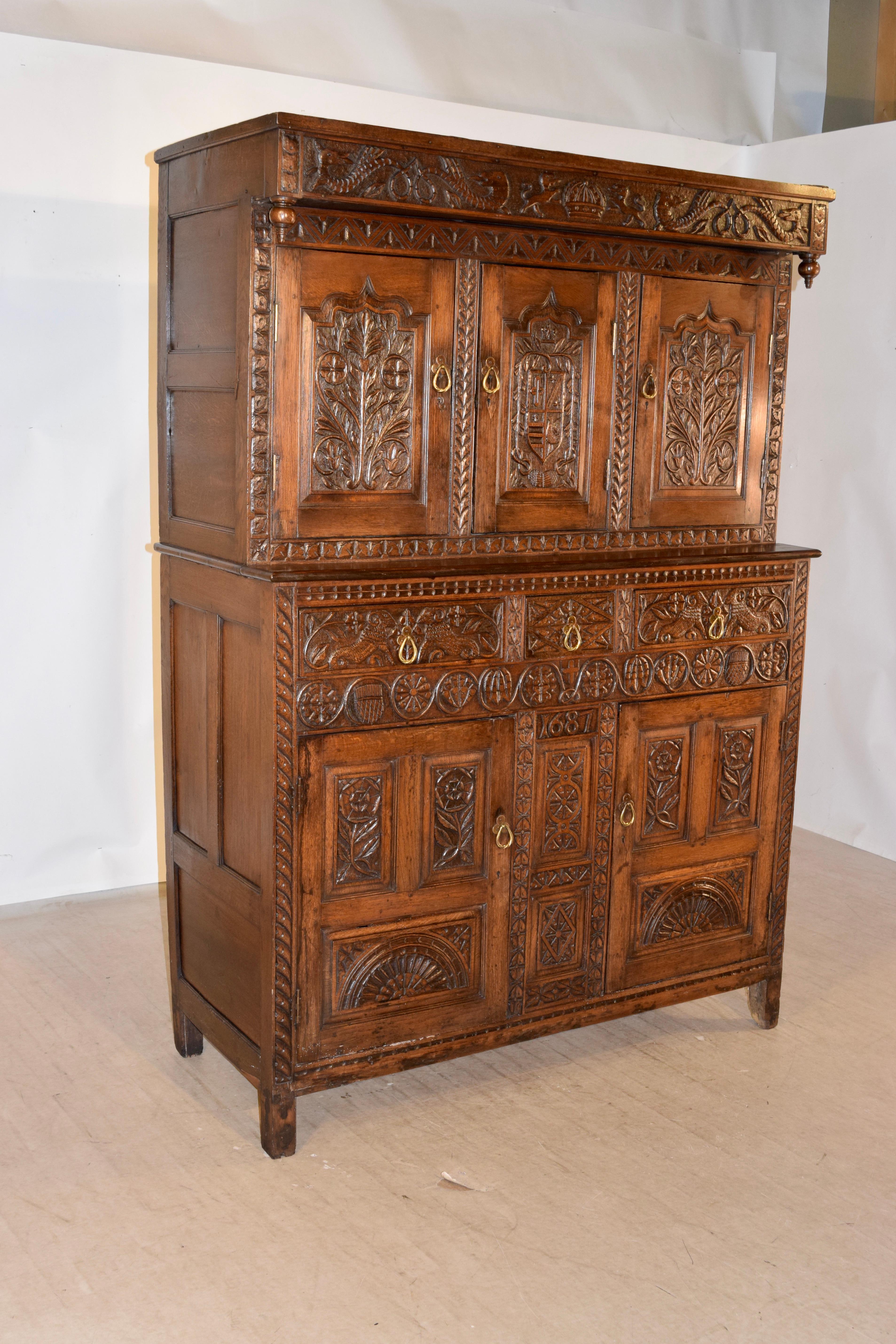 A late 17th century Charles II period carved oak court cupboard from England. The court cupboard breaks down into two sections; the upper section has a top rail boldly carved with a central crown flanked by lions and dragon motif, above a pair of