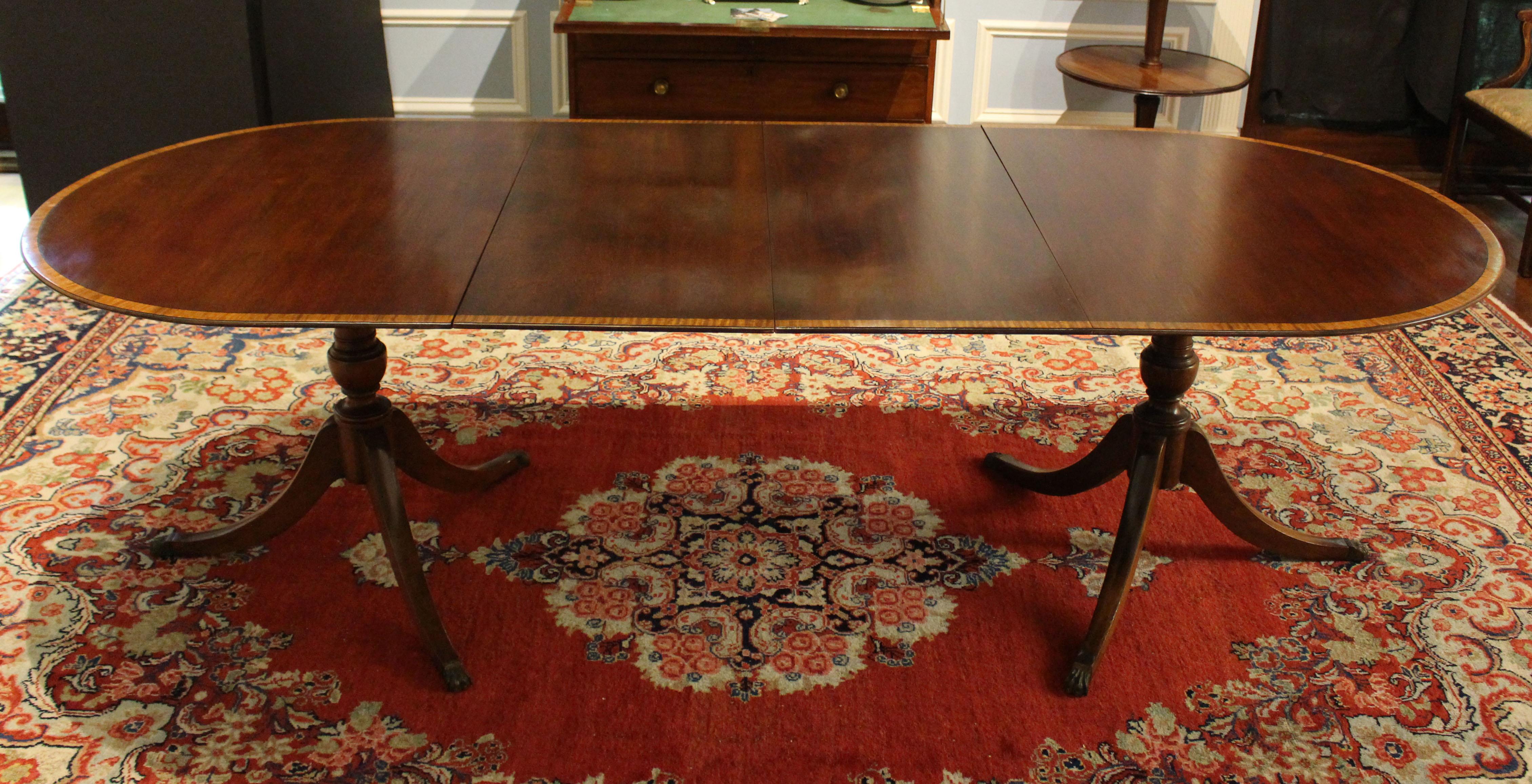 Dated 1953 Charak Furniture Co. double pedestal dining table. Label intact, Boston, Mass. 2 leaves. Mahogany with mahogany veneers, ebony stringing and satinwood crossbanding. Vasi-form pedestal shafts with 3 splay legs ending in lion paw caps. 42