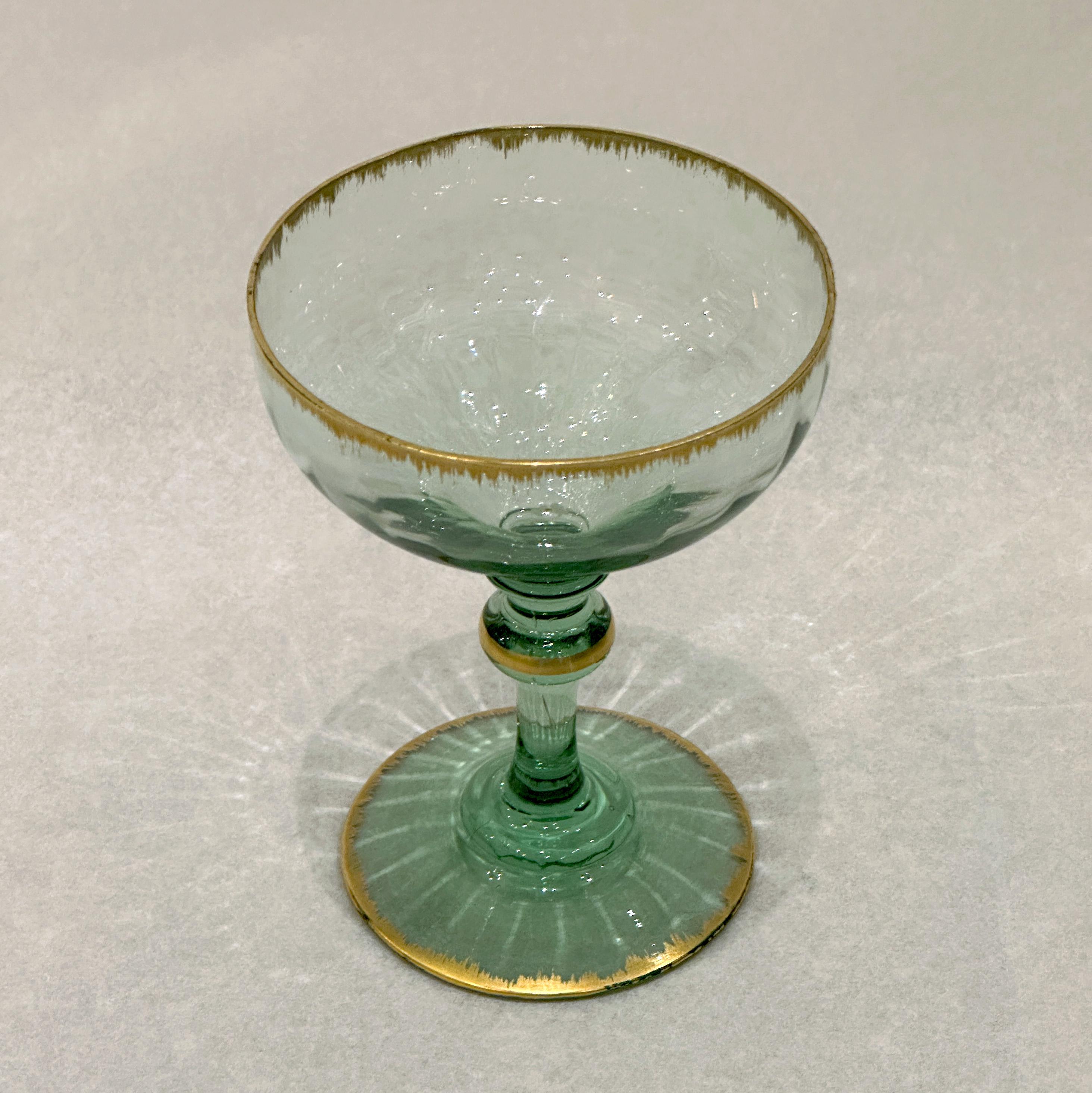 This emerald green-tinted blown glass wine glass exemplifies the exceptional craftsmanship of the Daum manufactory in Nancy around 1900. Its ribbed design lends a subtly animated texture, while delicate gold highlights - applied using the combed