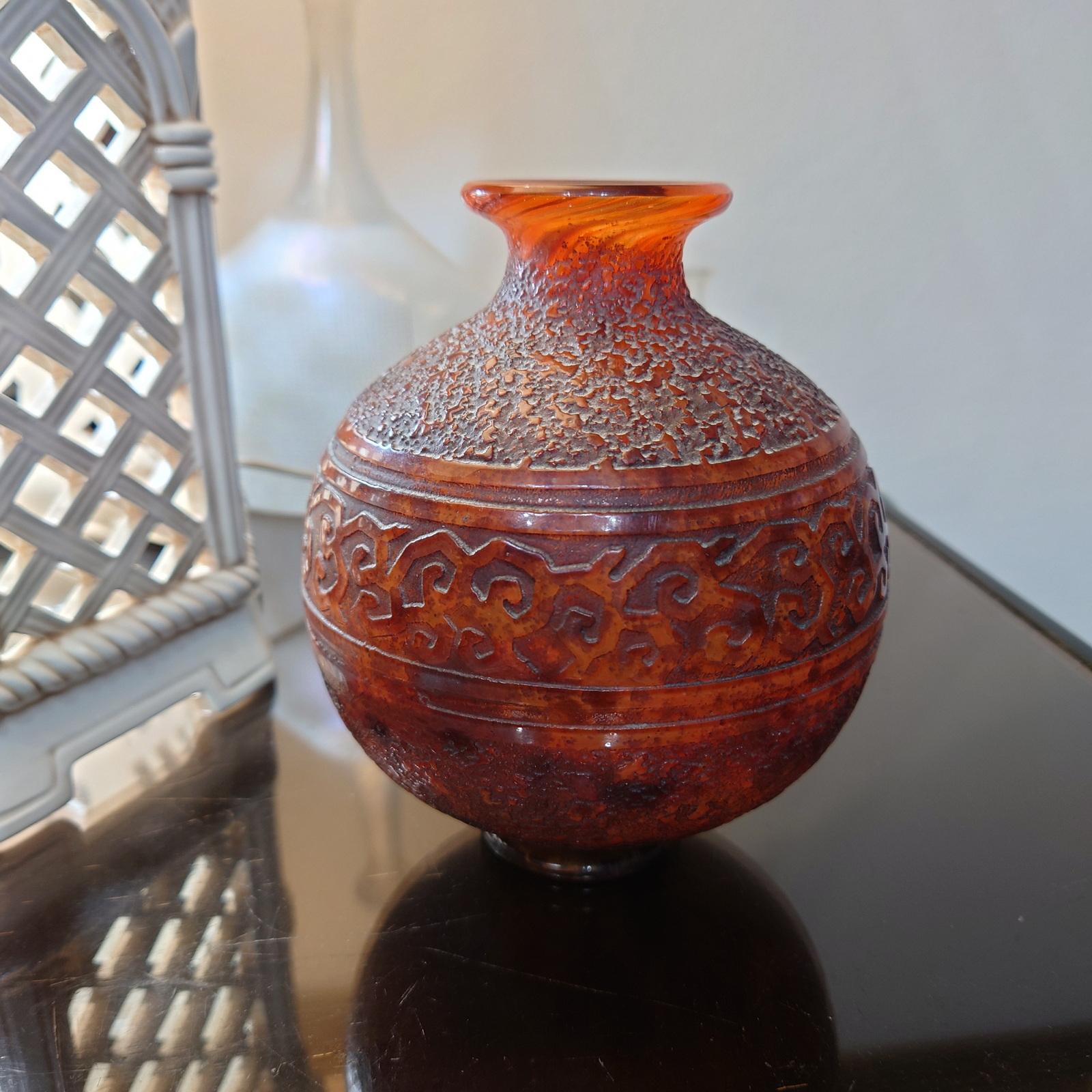 Vase en verre Art déco de Daum Nancy, en forme de boule, reposant sur une base ronde, avec une bouche étroite et évasée.
Ce vase boule est en verre teinté rouge-orange, décoré de poudres intercalaires brunes et gravé d'une frise de rinceaux sur un