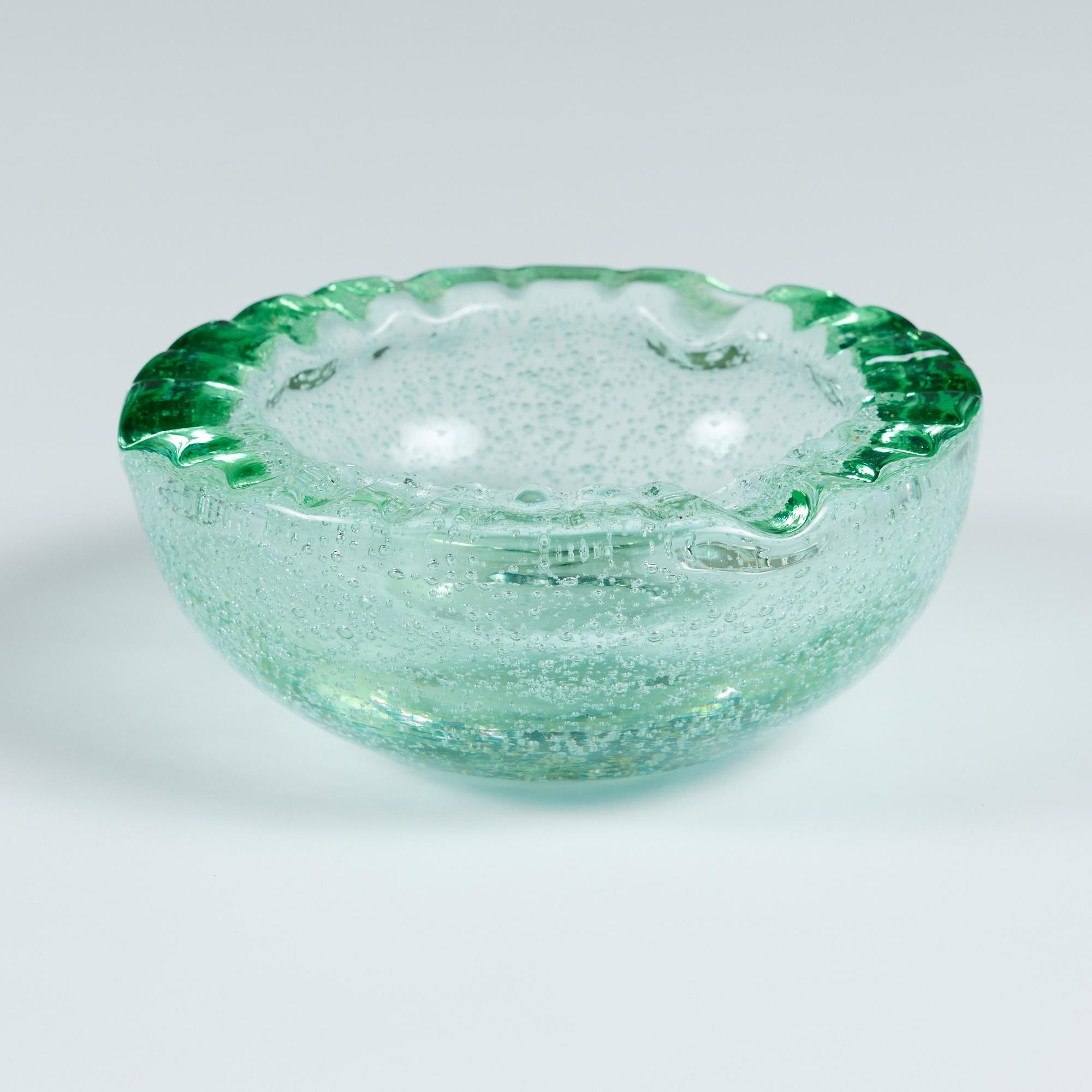 Round glass ashtray or catchall by Daum House which started in 1878 in Nancy, France. This piece, created in the mid 20th century, has an all over bubble throughout the green colored glass. The rounded dish has divots around the rim, perfect for a