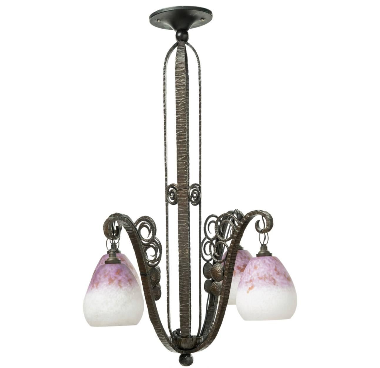 An Edgar Brandt style four light wrought iron chandelier with Daum Nancy glass shades each signed Daum Nancy with Cross of Lorraine. Shades are in pink, purple and cream variegated design. Art Nouveau - Art Deco French, circa 1930

Shades Engraved