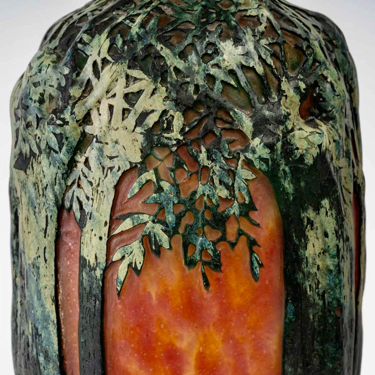 Multilayer blown glass vase decorated with trees in relief and a village cleared with acid and taken up with a wheel on a background of green, yellow and orange interlayer powders created by Daum between 1900 and 1905.

Engraved signature.

Perfect