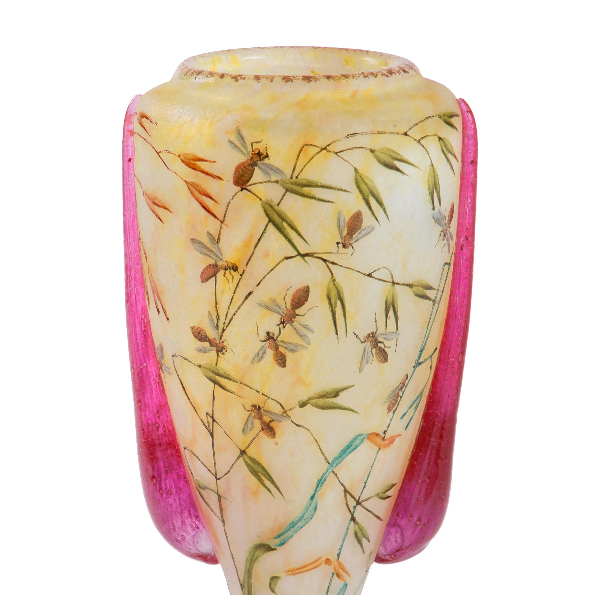 This French Art Nouveau Glass Vase by Daum features ruby-toned handles and bees buzzing amongst the variously colored foliage featured on the vessel. The vase utilizes the famous Daum Studio’s technique of blowing clear glass around an inner layer