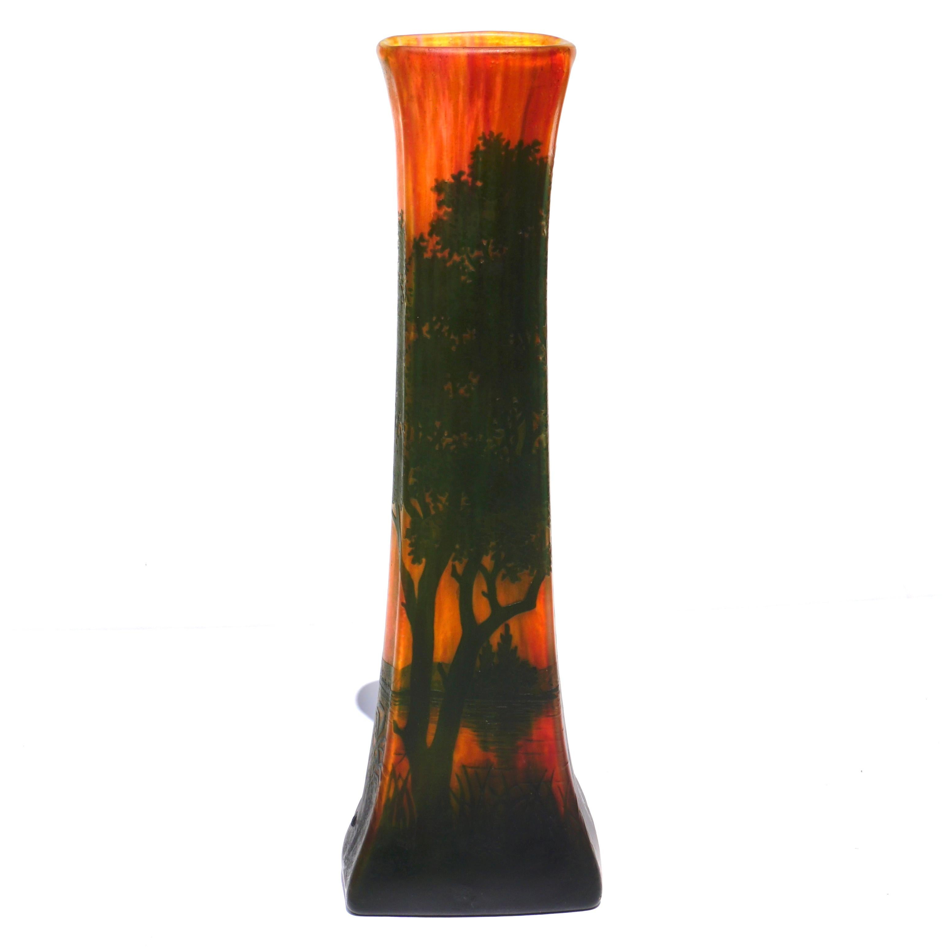 A warm scenic tall vase by Daum Freres from Nancy France circa 1900. The scene is a landscape with lake and green trees and bushes in the fore and back ground. The interesting feature of this four sided tapered vase in the yellow, orange and red