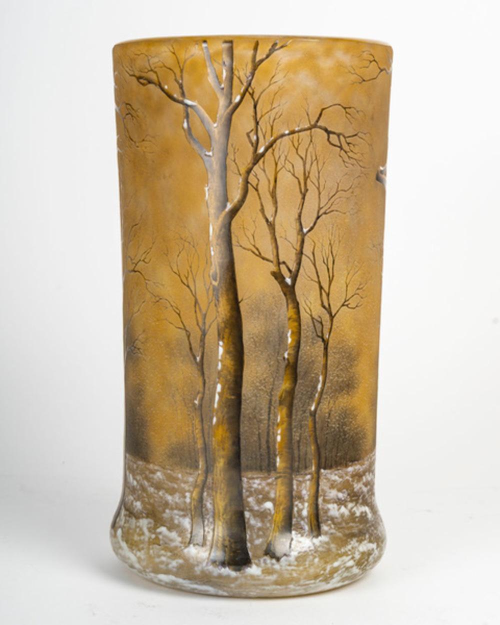 DAUM Nancy: Trees under the snow Double-layered tubular glass vase with an overflowing base. Decorated with acid-etched, hot-enamelled brown bare trees, snow-covered ground and trees painted in grisaille on a background speckled with yellow and