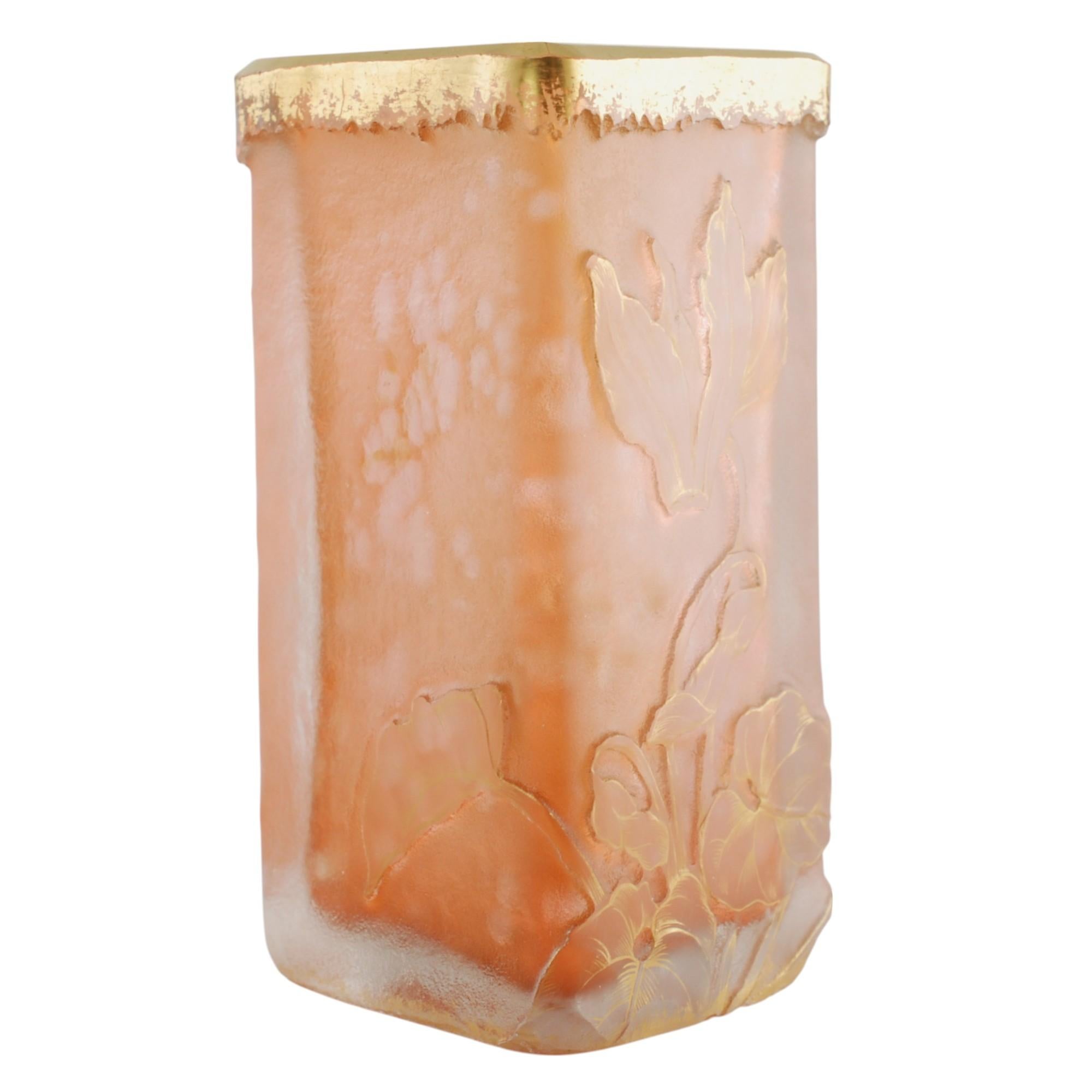 Este jarrón de vidrio artístico francés Daum Nancy tiene forma de vaso de diamante con un color rosa moteado y detalles dorados. El exterior de la pieza presenta una detallada decoración tallada a rueda consistente en una flor de ciclamen y follaje