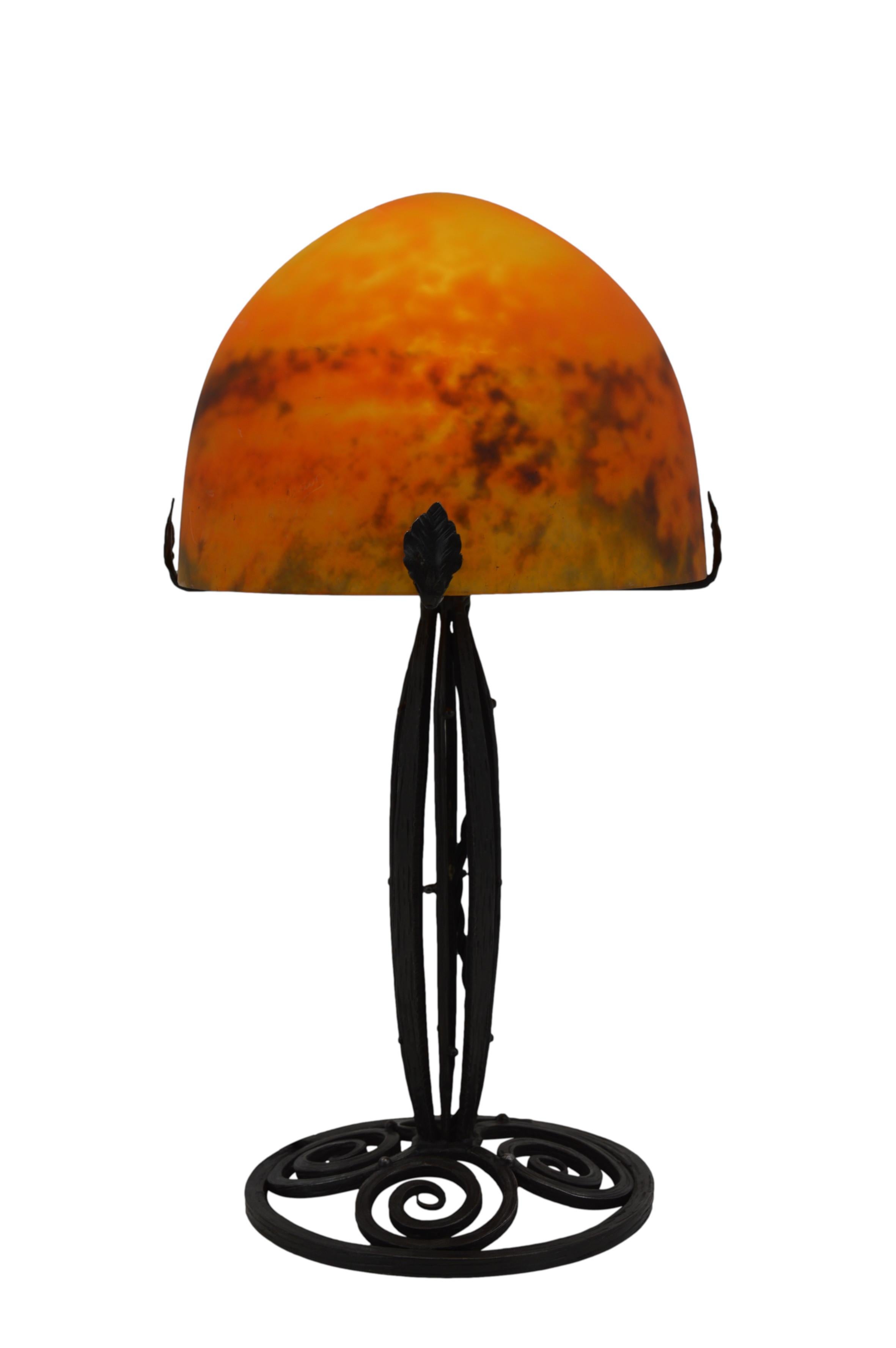 This beautiful French Art Deco table lamp, designed by Daum (Croismare) in France during the 1920s, features a stunning blown double glass shade paired with an elegant wrought iron base. The shade showcases a vibrant mix of orange, red, and dark