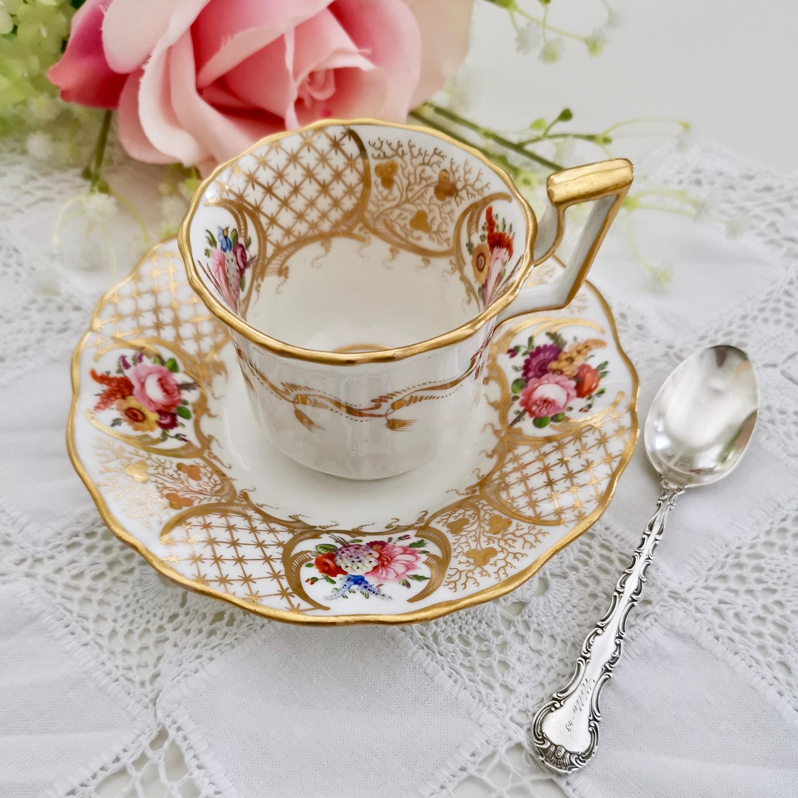 This is a beautifully decorated coffee cup and saucer made by Davenport in about 1825, which was the Regency era. The cup is white with a beautiful decoration of gilt and hand painted flowers, and it is shaped in the 