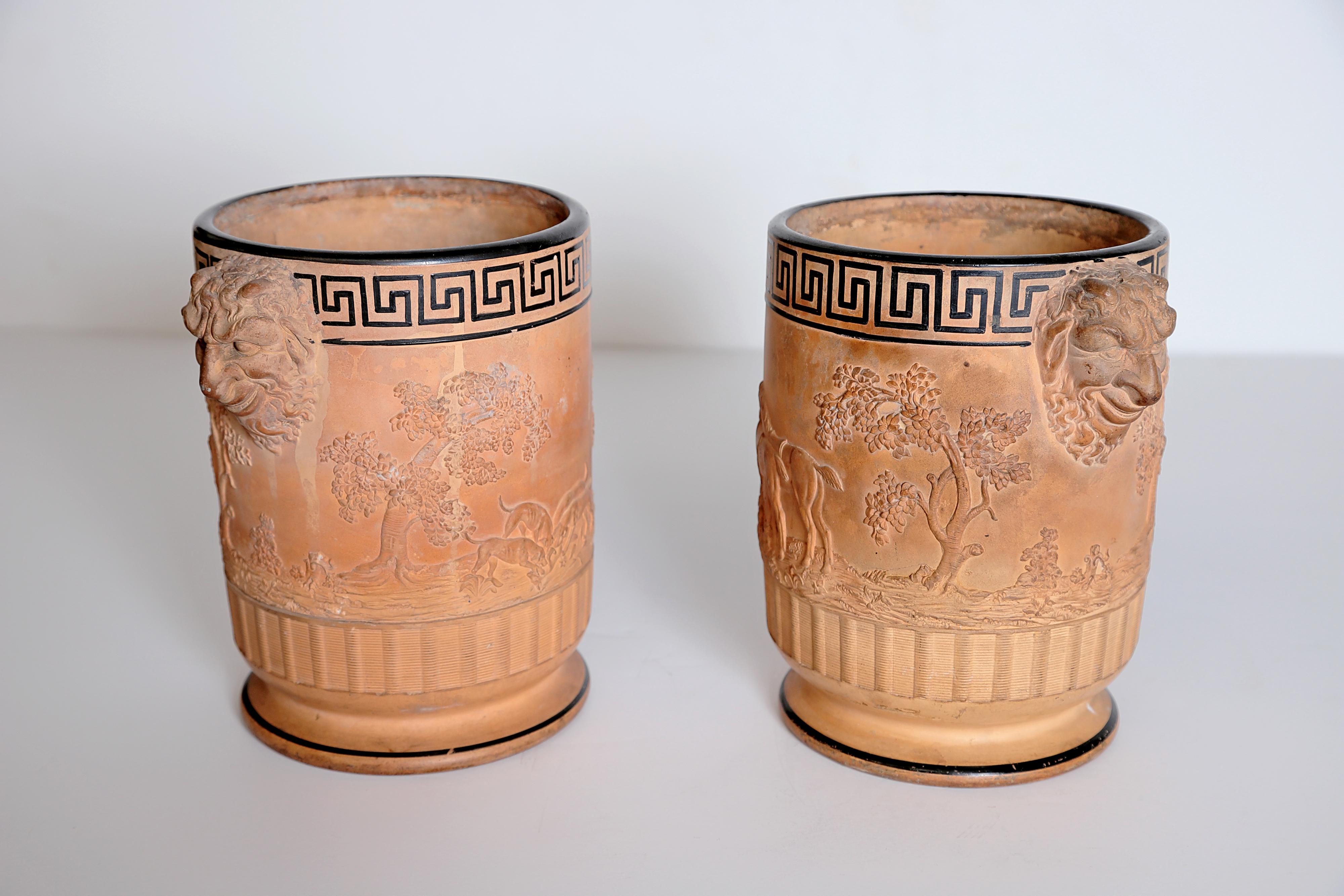 A near pair of Davenport terracotta wine coolers of barrel form with satyr handles, relief moulded with continuous hunting scenes, beneath brown enameled Greek key designs, the foot rims with engine turned bands, also enameled in in brown. Impressed