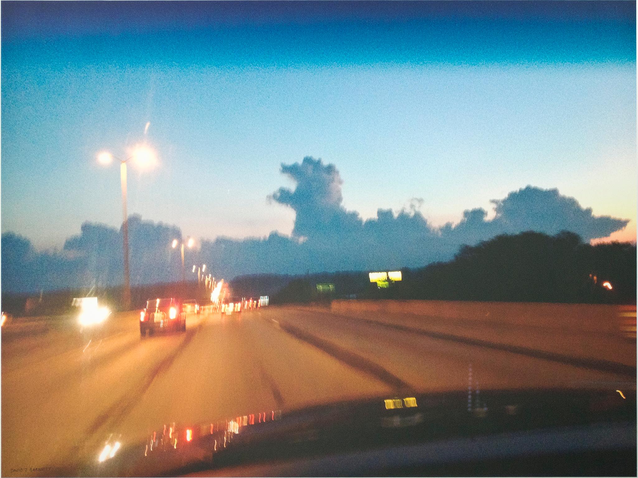 "Dashboard Sky Dragon" is an original photograph by David Barnett, signed in the lower left. The photo was taken during a commute when the artist was struck by the cloud formations as the sun sank behind them. The foreground is allowed to blur with