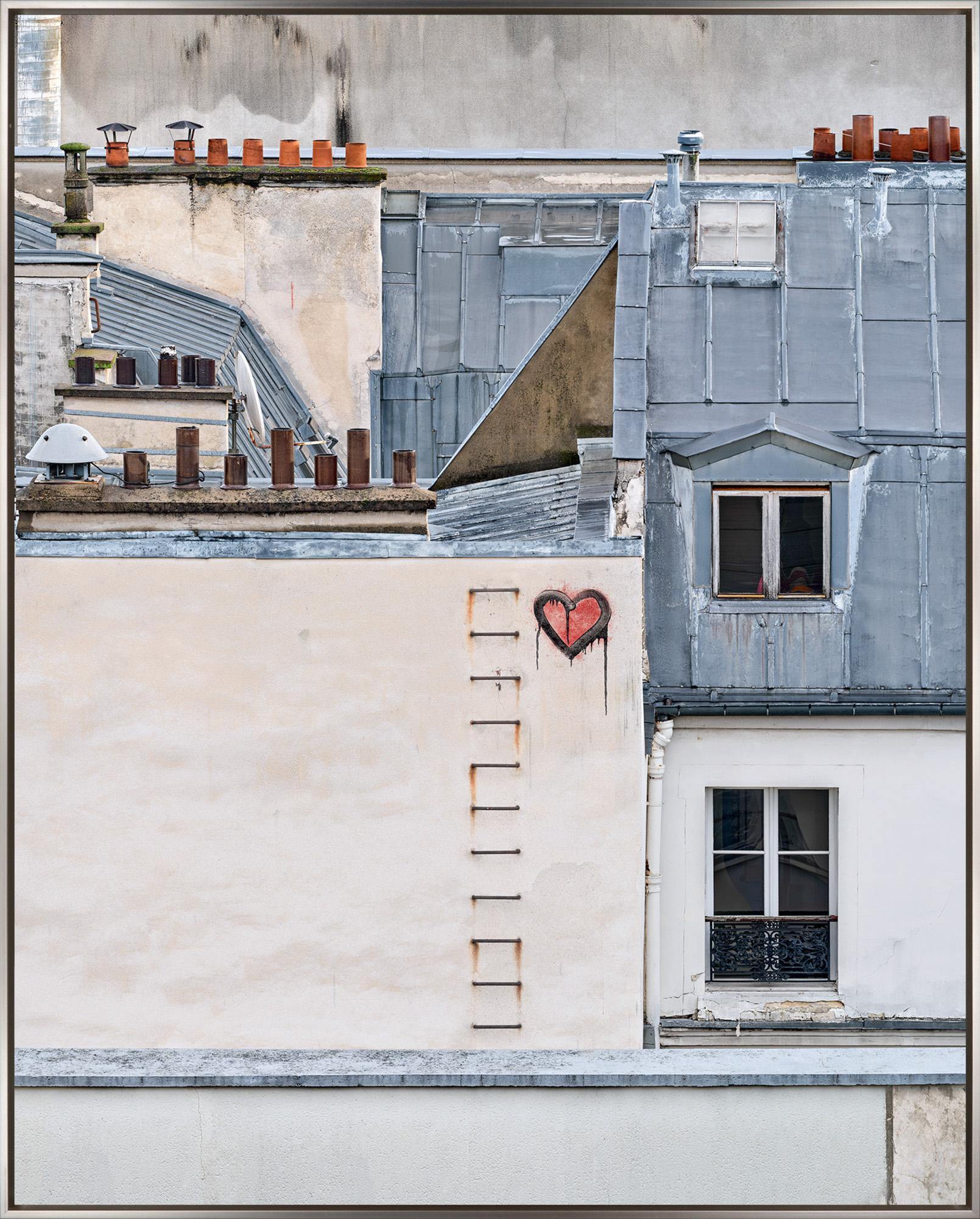 "Amore, Paris, France" is a framed photograph (archival dye infused print) on aluminum by David Burdeny, depicting buildings in Paris with a graffitied heart symbol spray-painted near the center of the composition. The iconic architecture of