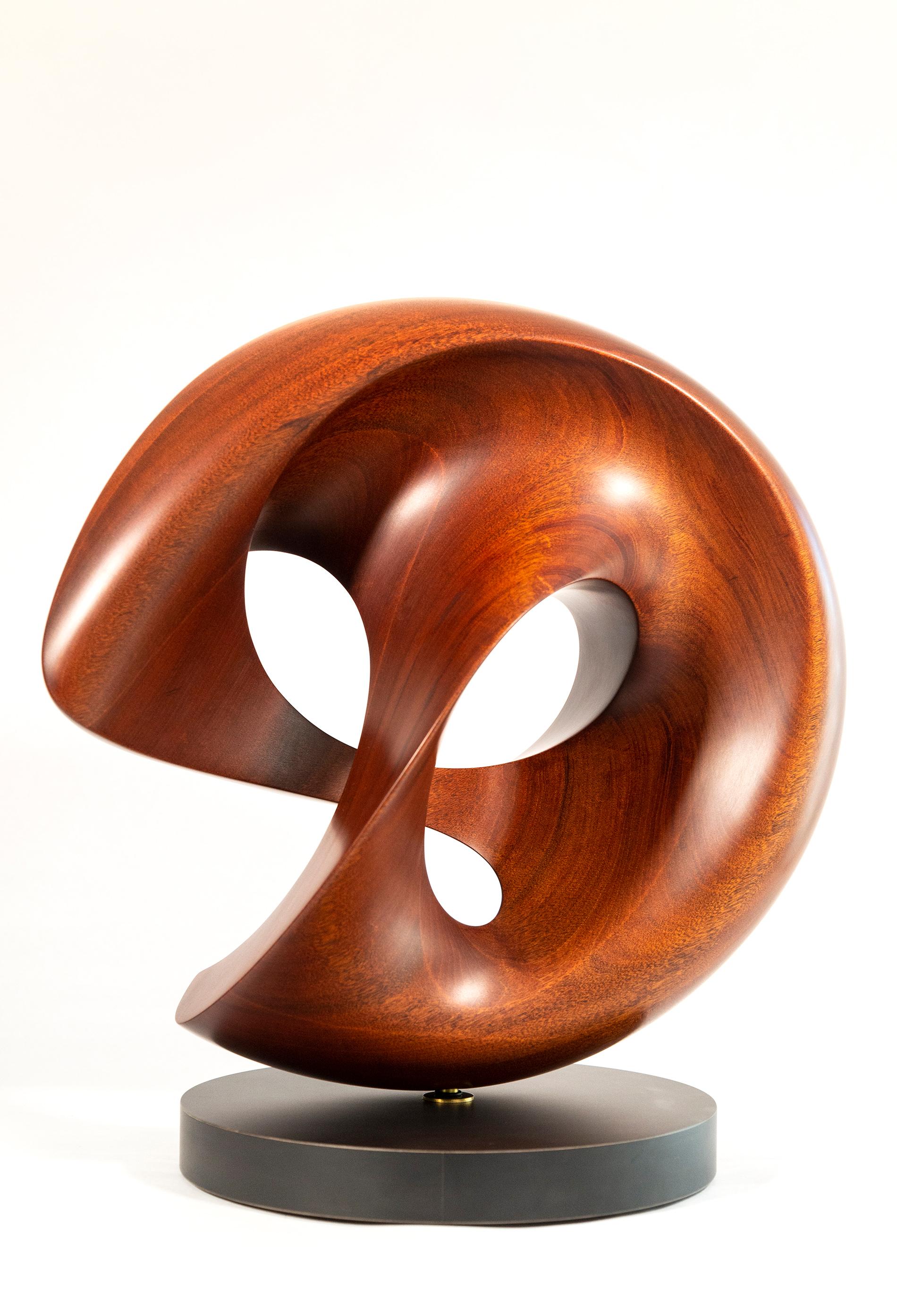 The elegant, lyrical curves of this abstract sculpture by David Chamberlain are hand-carved from one continuous loop of mahogany wood. The American artist is a sculptor, painter, jazz musician, a Capella singer, composer, writer and educator—a