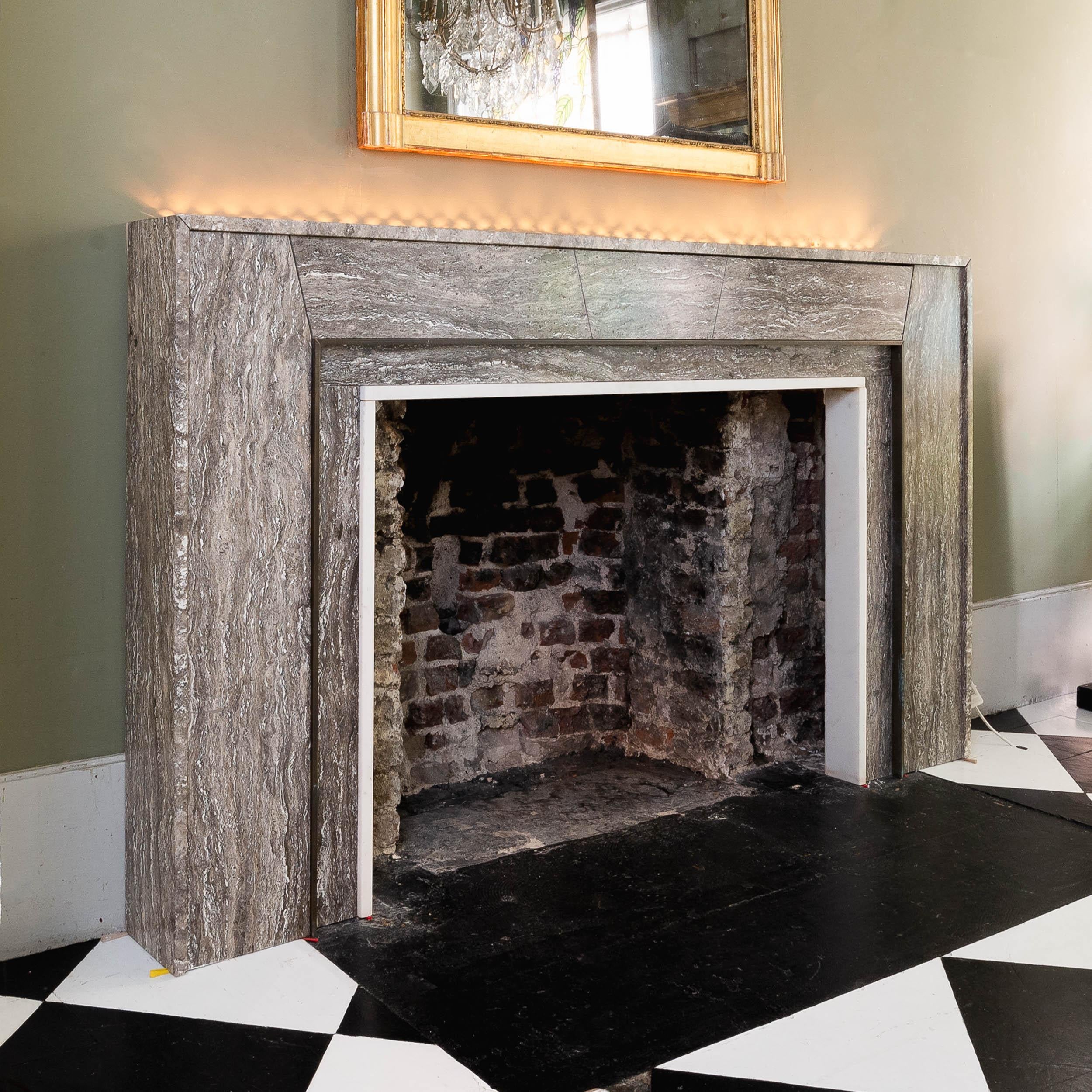A contemporary brown travertine, bronze and statuary marble fireplace removed from the London residence of renowned interior decorator David Collins, the illuminated strip to the rear of the shelf covered in bronze hatching, the frieze centred by