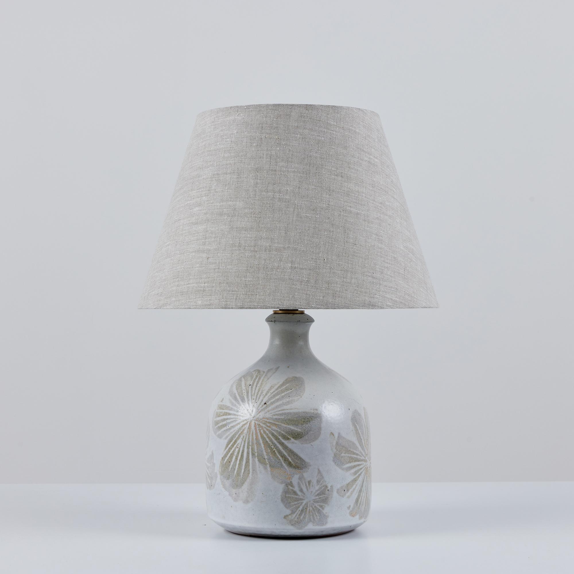 David Cressey ceramic lamp, circa 1960s, USA. The wheel thrown ceramic lamp features a speckled grayish blue colored glaze with applied floral detailing in a gray-brown tone. The newly rewired lamp features new light gray linen shade. The shade and