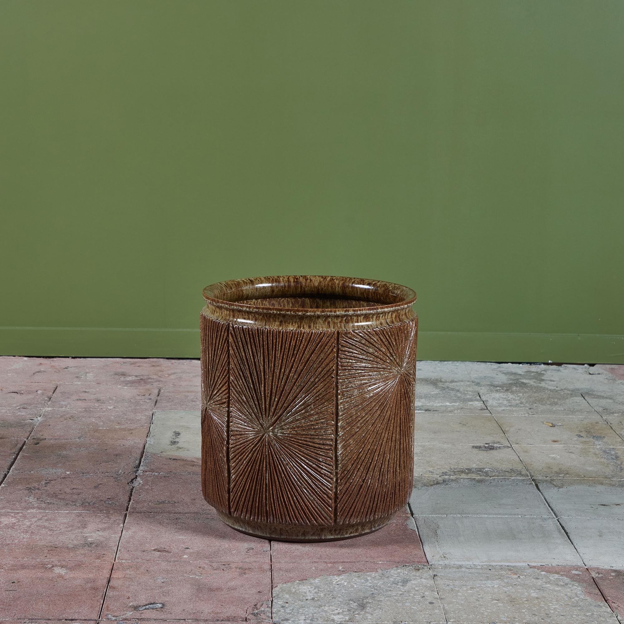 A cylindrical stoneware planter from Robert Maxwell and David Cressey's 1970s collaboration Earthgender. The planter has a rounded lip and an incised all-over sunburst pattern. The interior and exterior of the planter are covered in a speckle taupe