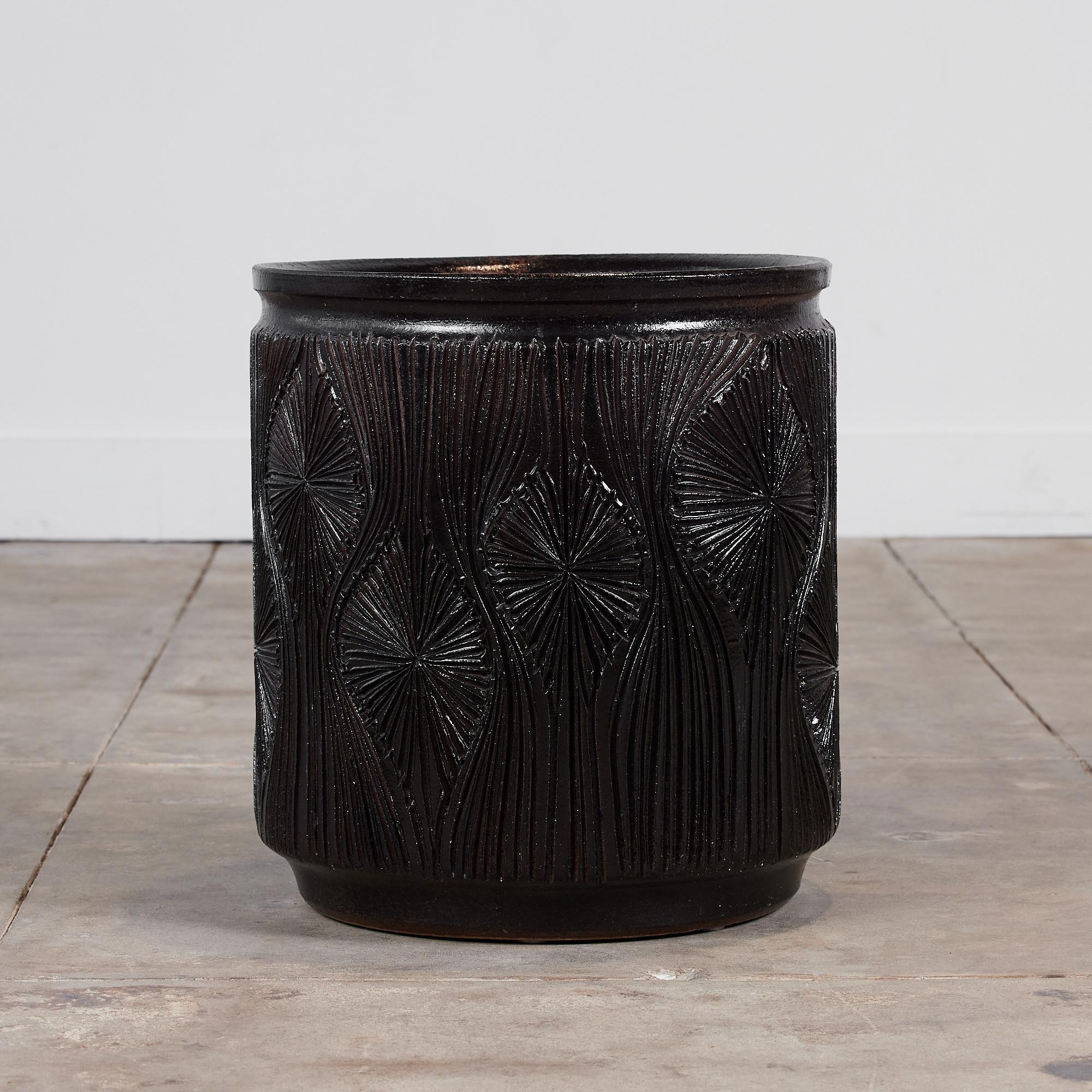 A cylindrical stoneware planter from Robert Maxwell and David Cressey's 1970s collaboration Earthgender. The planter has a rounded lip and an incised all-over teardrop sunburst pattern. The interior and exterior of the planter are covered in a dark