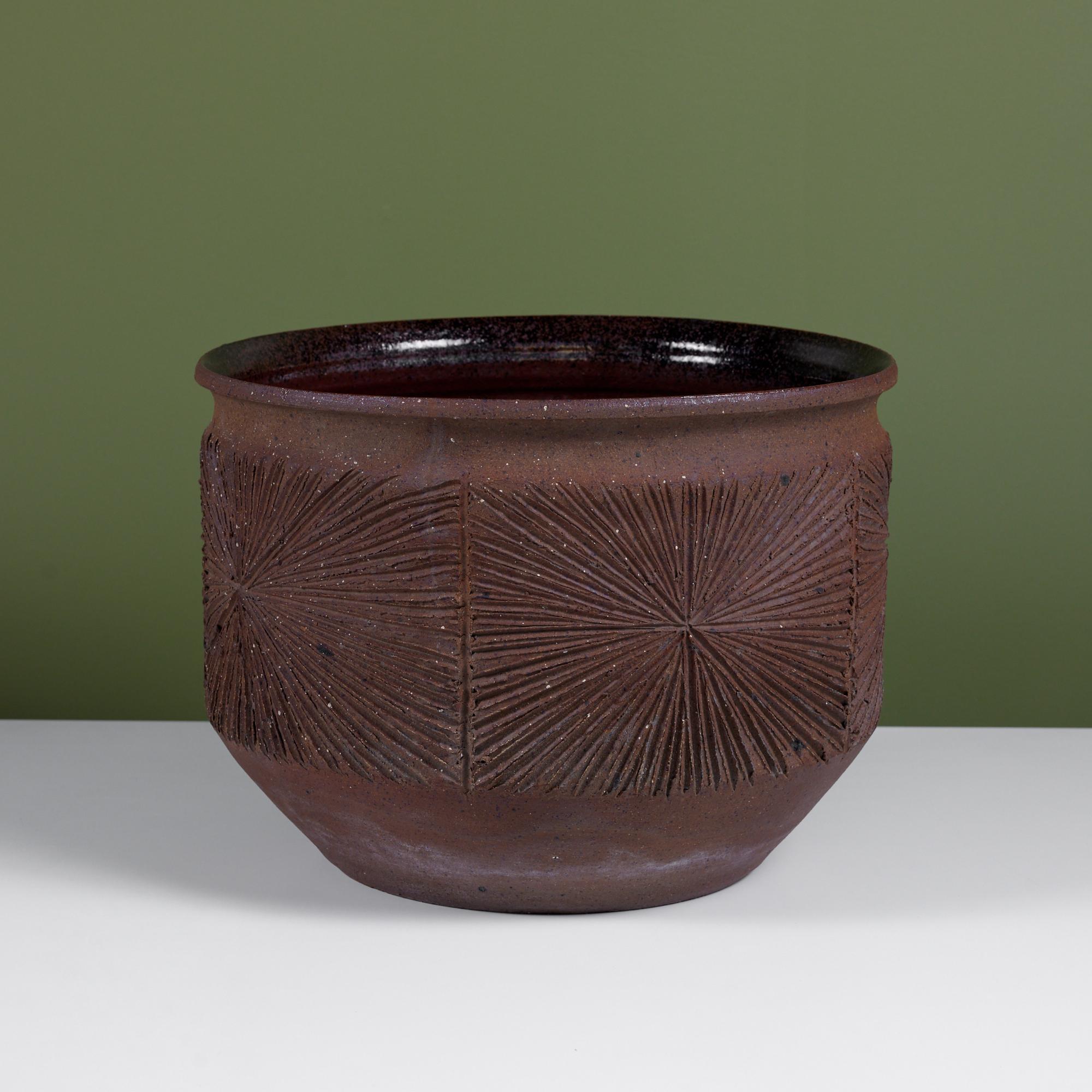 An unglazed stoneware bowl planter from David Cressey and Robert Maxwell's 1970's collaboration, Earthgender. The planter has a rounded lip with a dark speckle glazed interior, an incised all-over pattern in the 