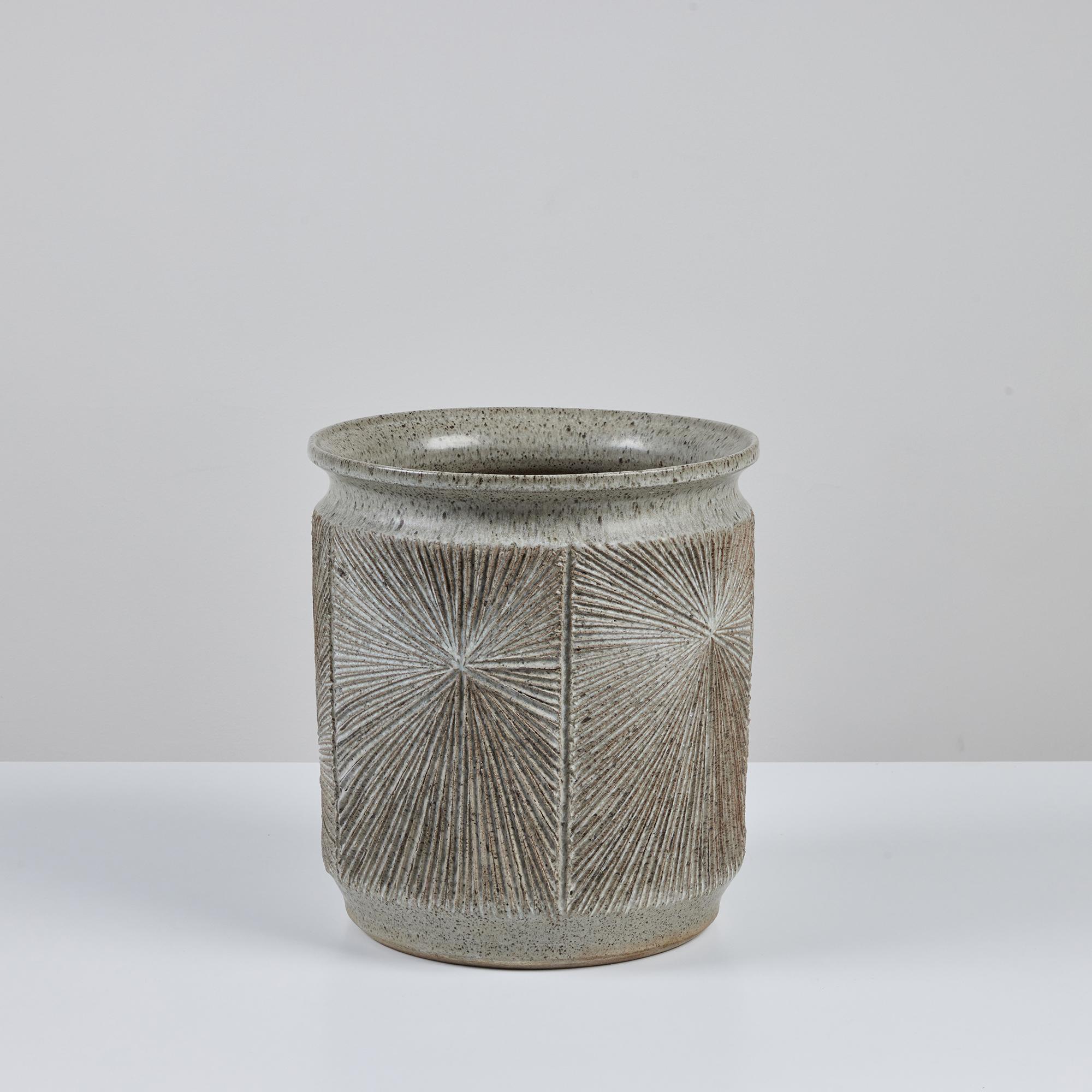 A cylindrical stoneware planter from Robert Maxwell and David Cressey's 1970s collaboration Earthgender. The planter has a rounded lip and an incised all-over sunburst pattern. The interior and exterior of the planter are covered in a speckle cream