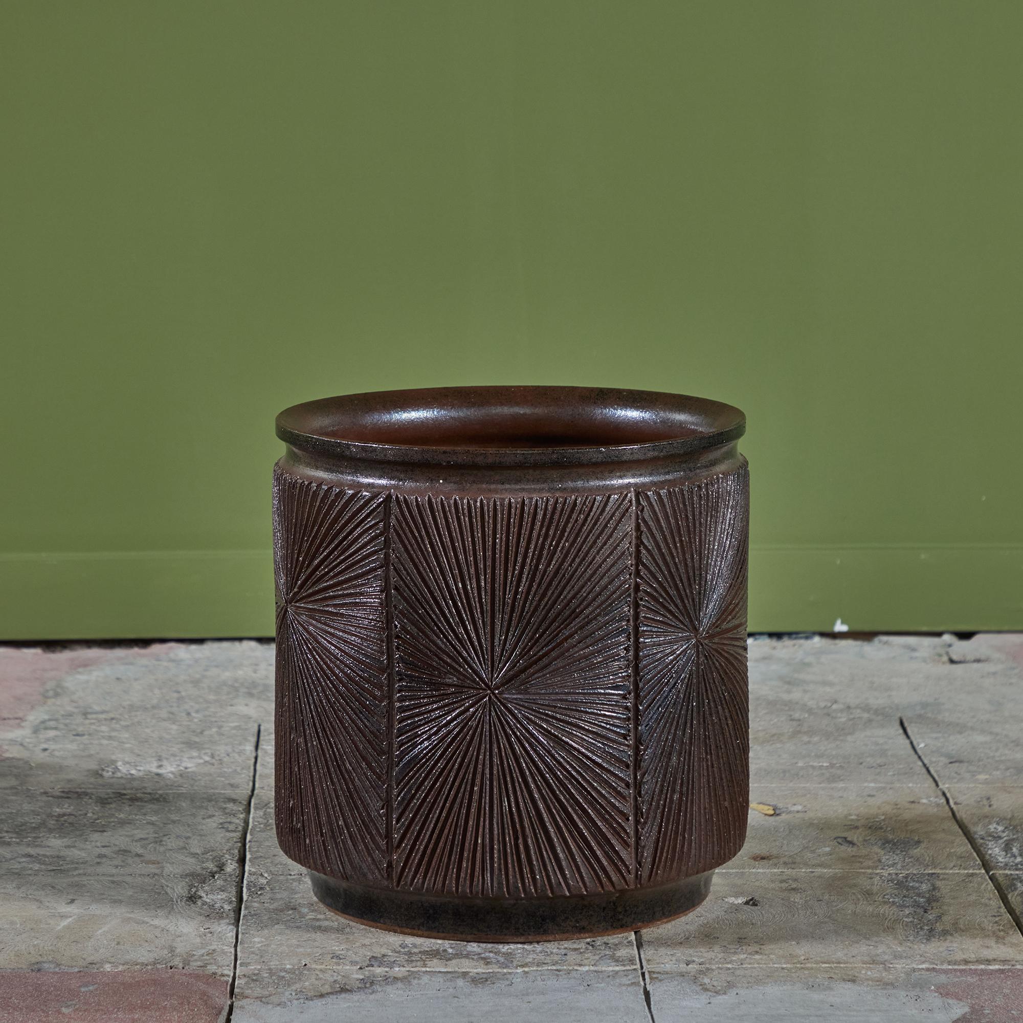 A cylindrical stoneware planter from Robert Maxwell and David Cressey's 1970s collaboration Earthgender. The planter has a rounded lip and an incised all-over sunburst pattern. The interior and exterior of the planter are covered in a dark brown and
