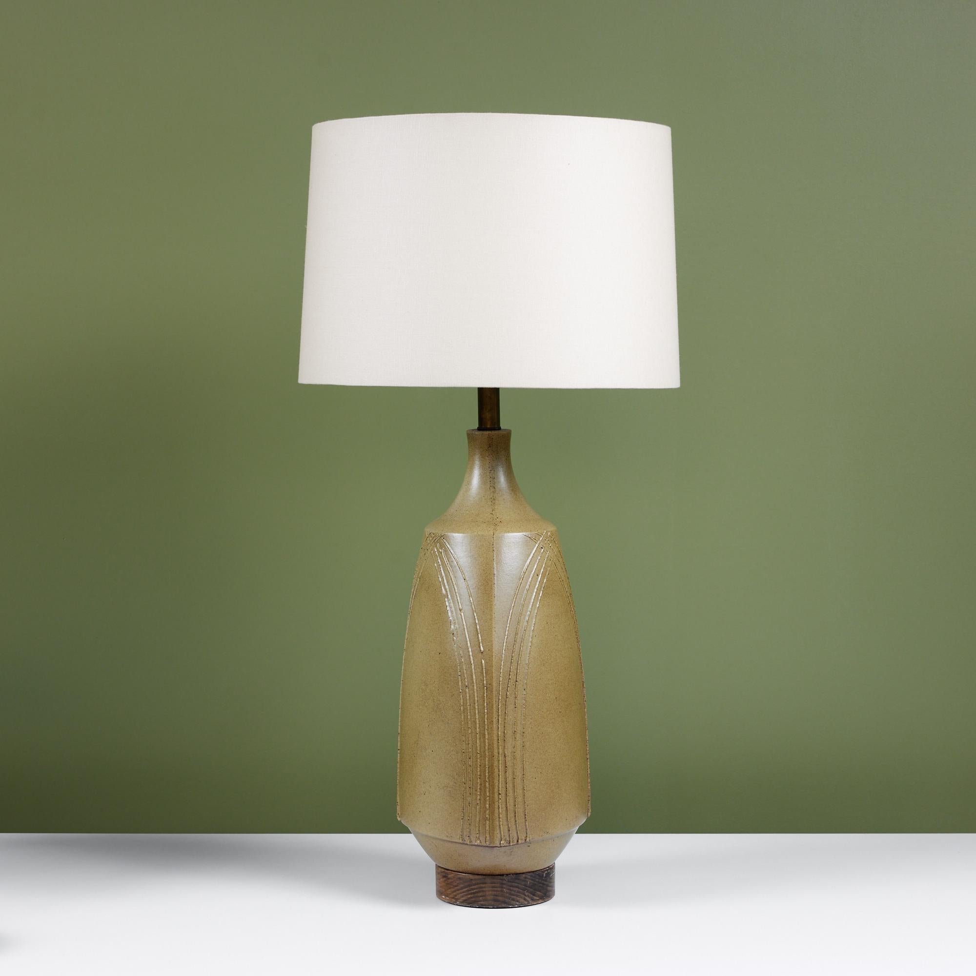 David Cressey stoneware lamp, c.1960s, USA. The wheel thrown stoneware lamp features an olive green speckled glaze with applied textured lines that intersect at the top of the lamp creating a triangular arch detail. The ceramic form sits atop a
