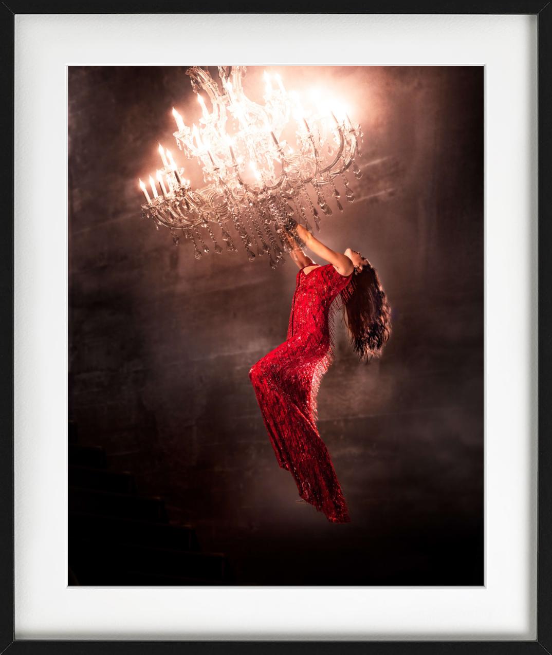 A woman wearing a red dress hangs on by a chandelier in a theatrical way, photographed by David Drebin.

All prints are limited edition. Available in multiple sizes. High-end framing on request.

All prints are done and signed by the artist. The