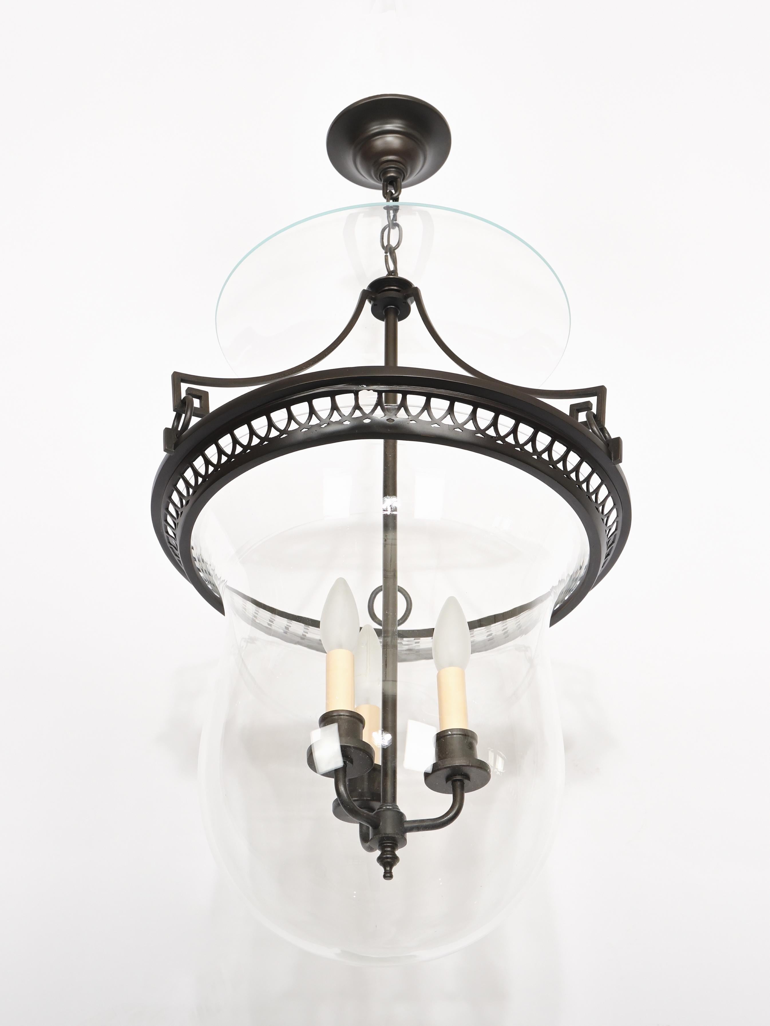 A custom ceiling lantern featuring darkened bronze Greek fret motifs and ornate frieze comprising the frame, with hand blown glass bell and dish, fitted with three light bronze cluster.

With three medium sockets (maximum total wattage 300 watts).