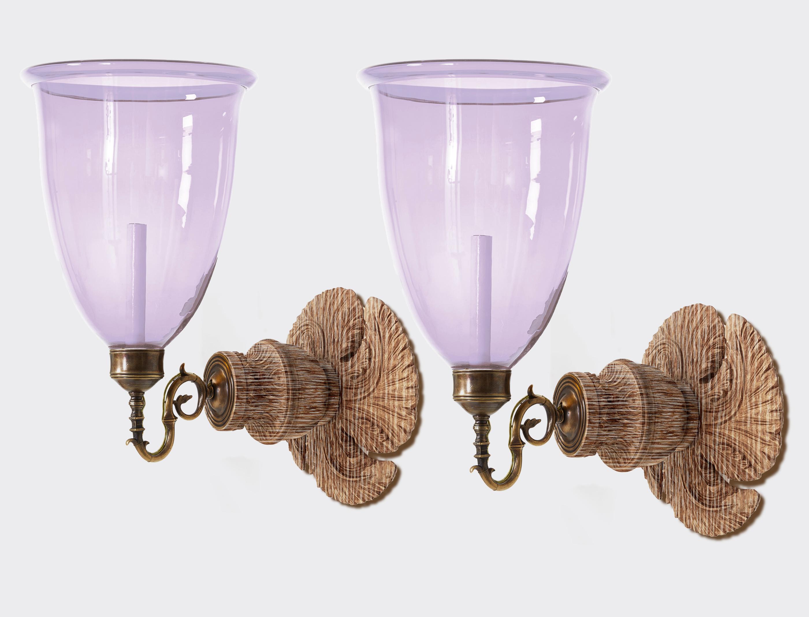 A pair of hand-carved gilt Georgian-styled backplates with patinated brass sconce fittings and large hand-blown lilac glass hurricane shades. Electrified with one candelabra base socket per sconce. Maximum wattage 60 watts incandescent 100 watts