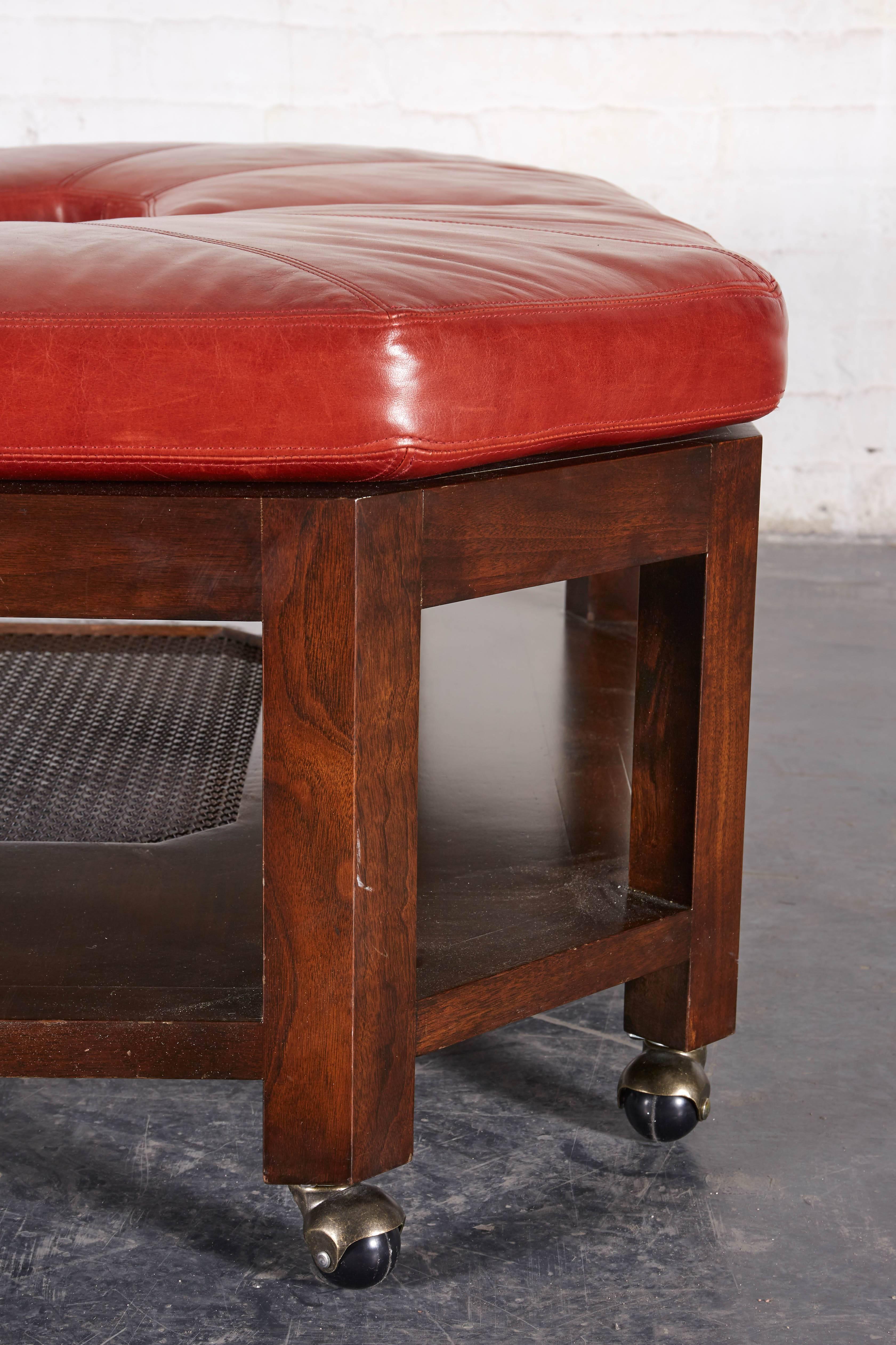 The square top with canted corners surmounted by four leather removable cushions; raised on straight legs joined by a platform shelf centered by a wire recess; on brass casters.