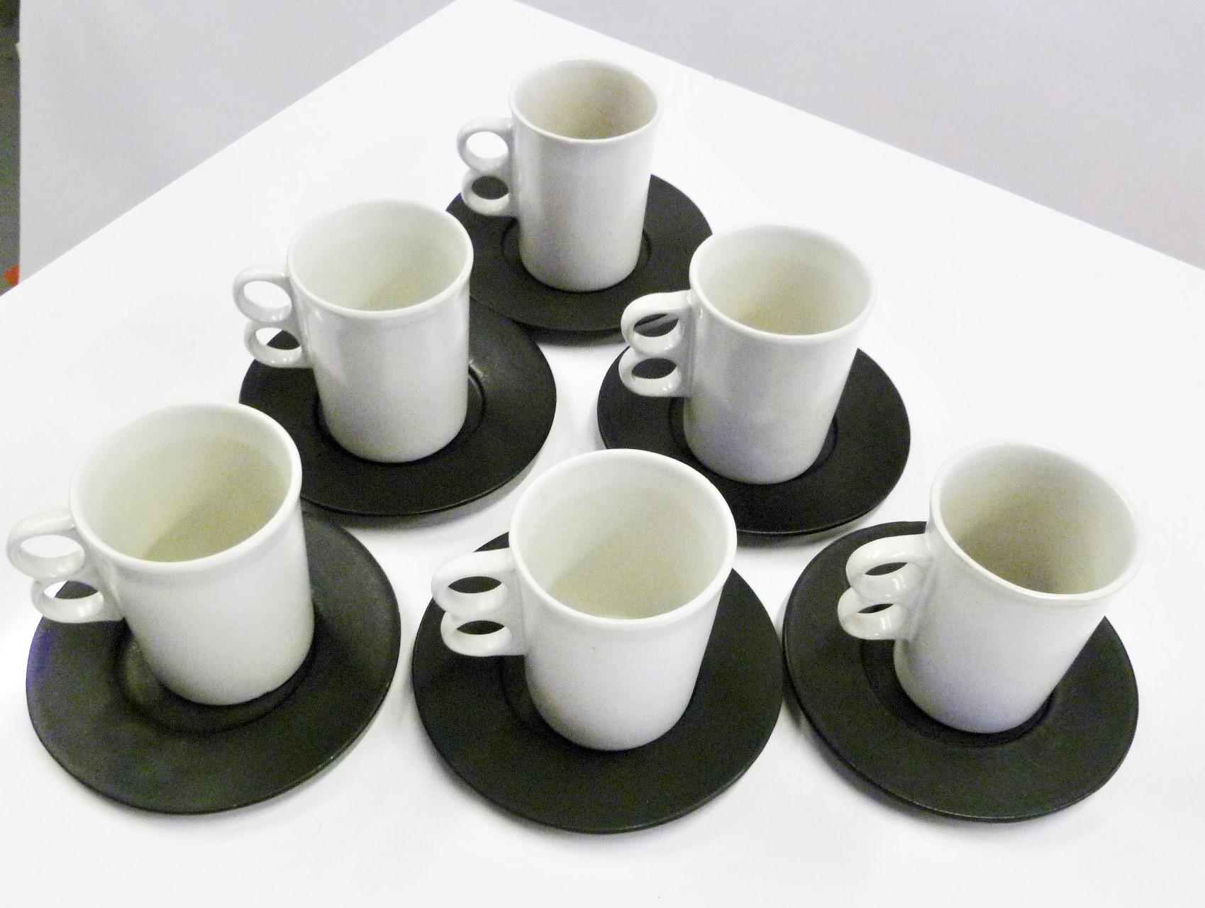 Designed by David Gil (1922-2002) for his company Bennington Potters of Vermont, a set of 6 matte white trigger mugs #1340 and 6 matte black plates/saucers. These are handmade stoneware pieces from the 1960s, each will be an individual creation thus