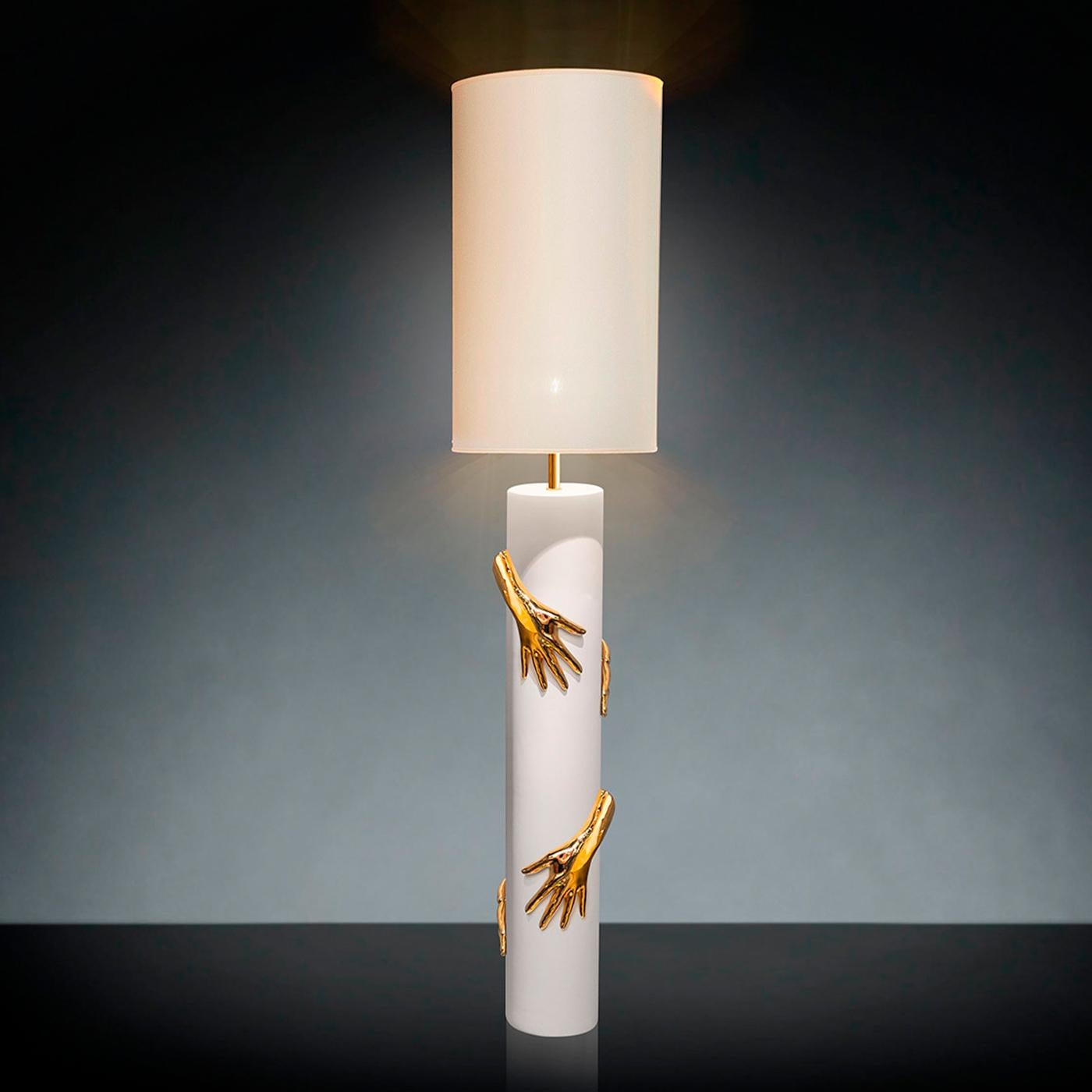 Featuring a captivating composition of polished gold and white ceramic, this superb floor/table lamp combines a minimalist silhouette with a relief insert in the shape of four hands almost looking alive as they embrace the cylindrical stand. The 24k