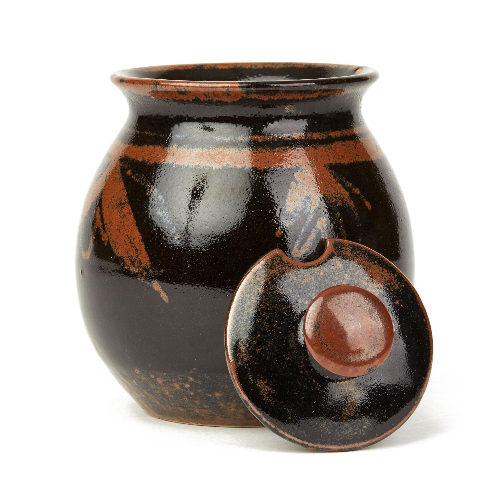 A very finely made studio pottery lidded conserve jar decorated in tenmoku glazes with a ribbon and bow pattern applied around the body of the jar by Scottish based potter David Heminsley (1927-2007). The stoneware jar is of rounded bulbous shape