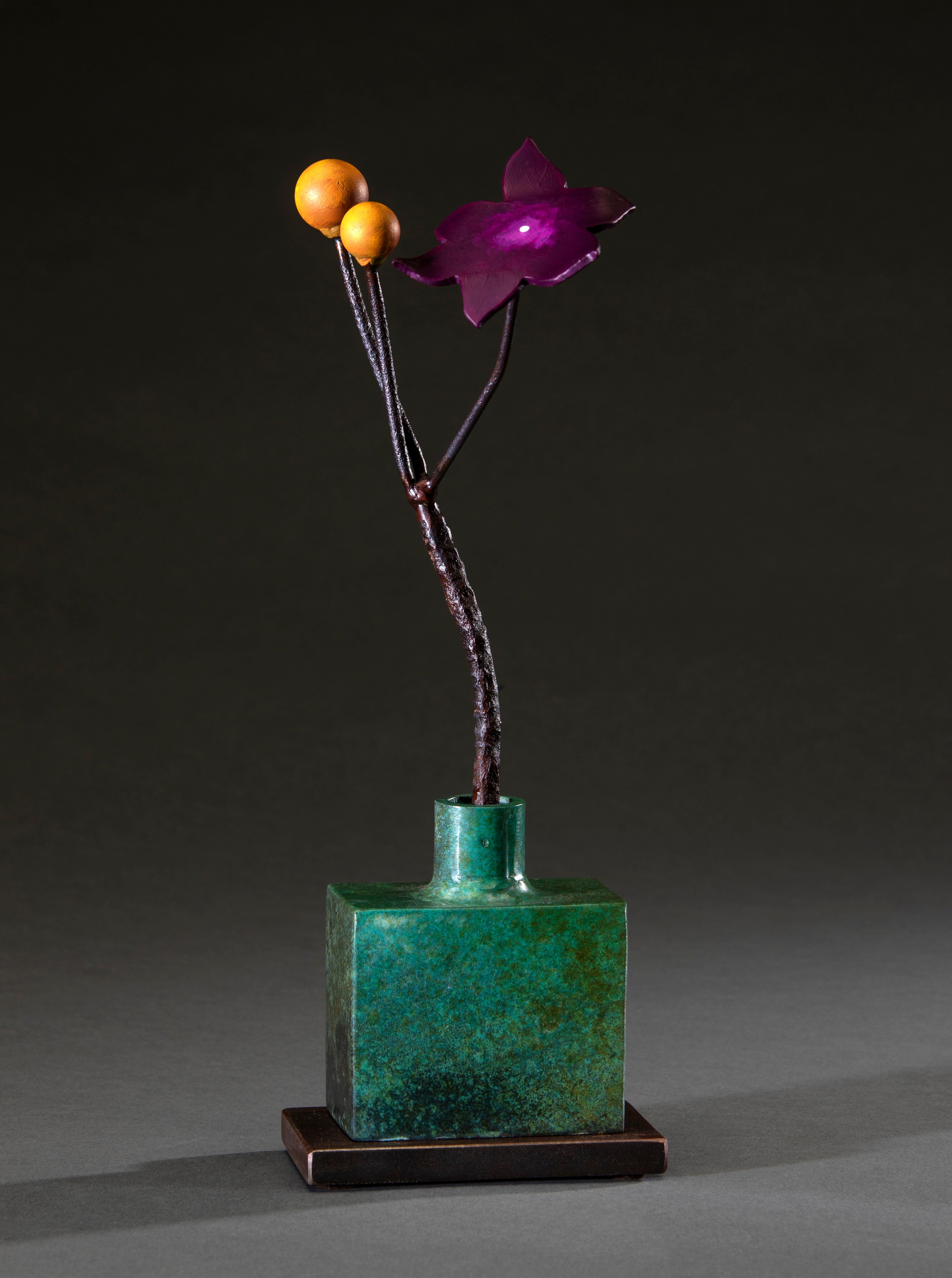 'Green Bottle Ochre Seeds' by David Kimball Anderson, 2022. Bronze, steel, and paint, 16 x 6 x 5 in. This sculpture features a  square vase cast in bronze and finished with a green patina. It features a steel flower painted in purple with two yellow