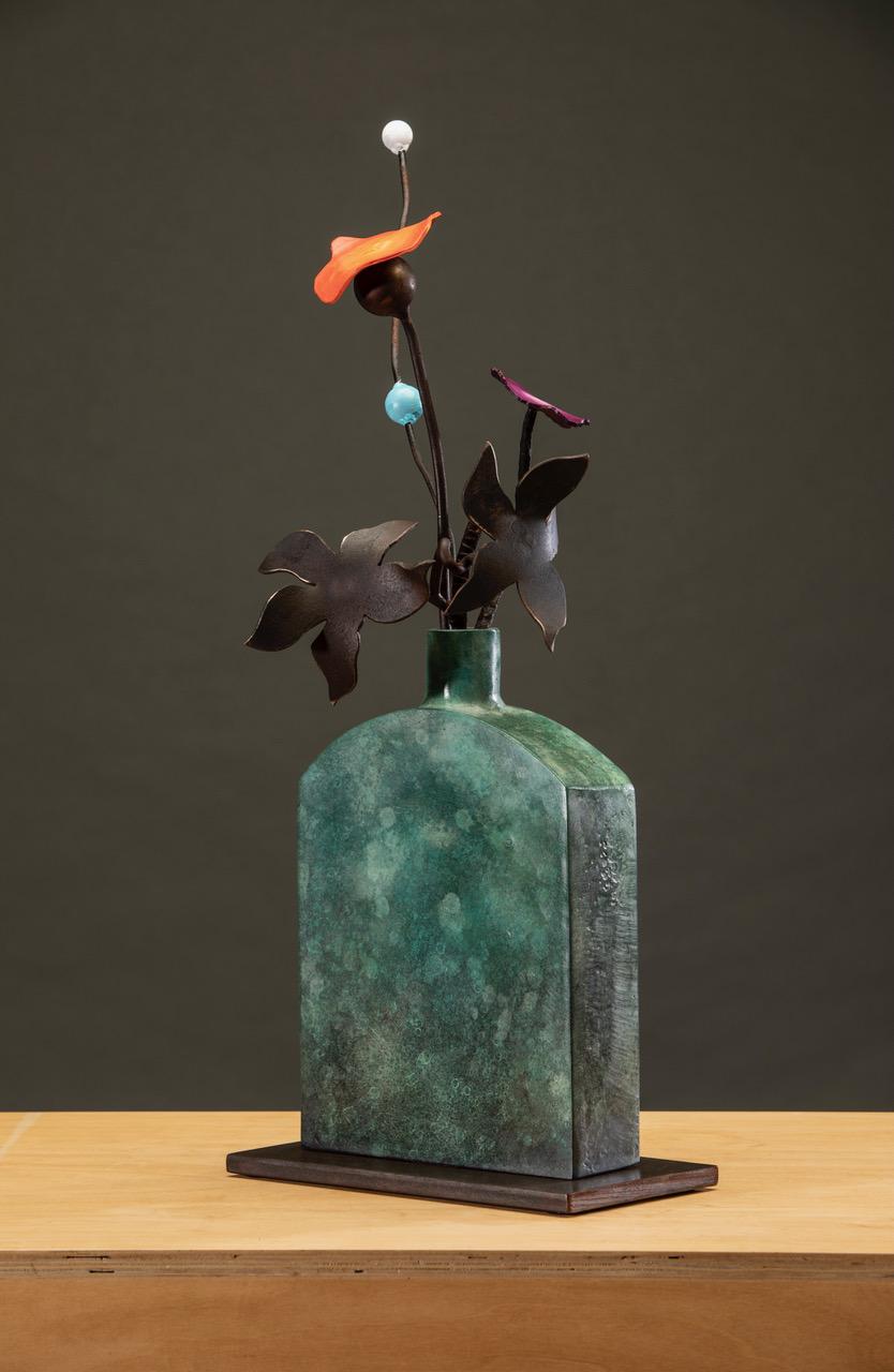 'Blue Bottle Summer' by David Kimball Anderson, 2021. Bronze, steel, and paint, 21 x 12 x 10 in. This sculpture features a rounded square vase cast in bronze and finished in patinas of green. It features two steel flowers, and two painted flowers in