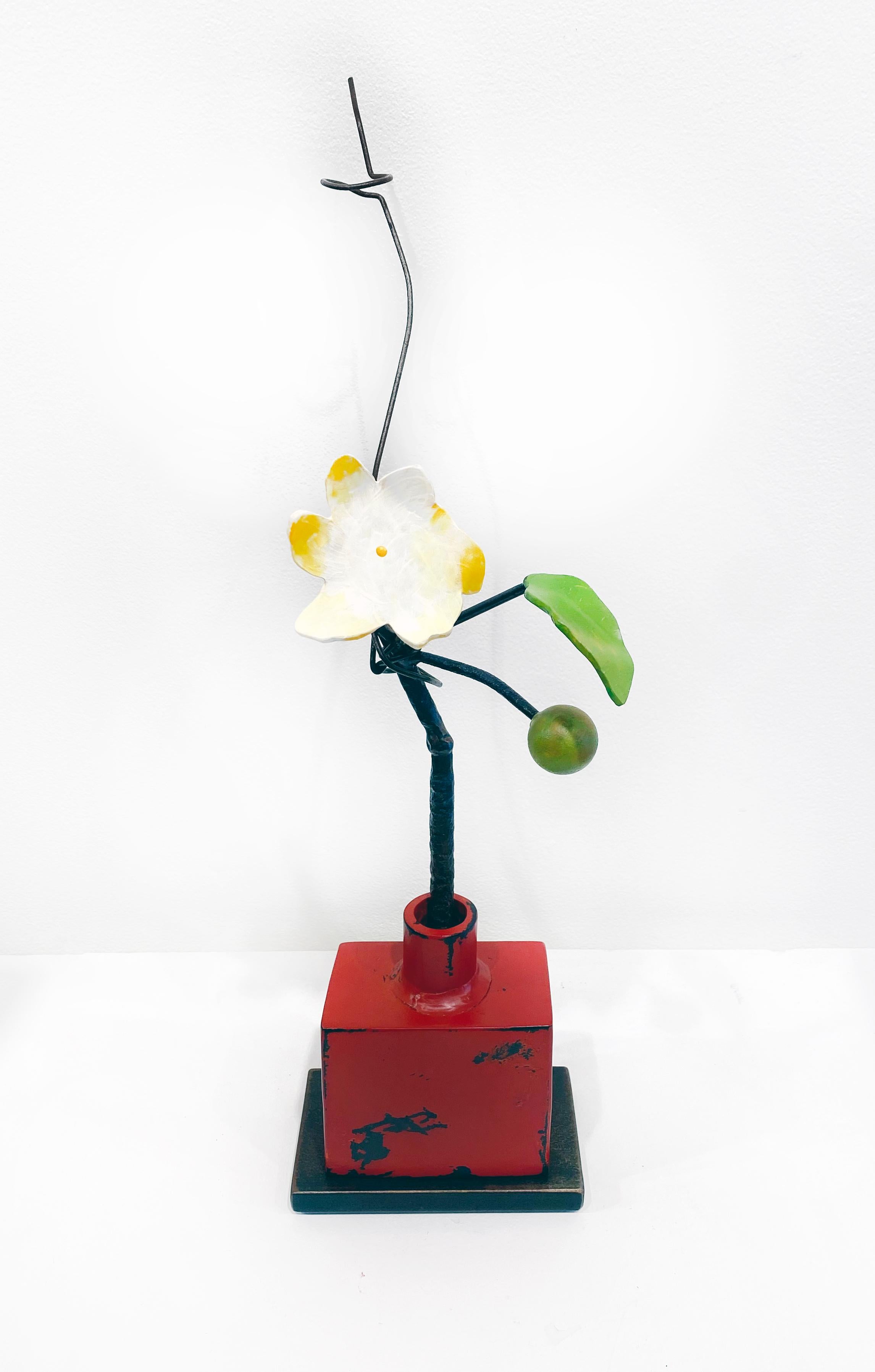 'Red Bottle Yellow Flower' by David Kimball Anderson, 2022. Bronze, steel, and paint, 18 x 8 x 6 in. This sculpture features a square vase cast in bronze and painted with red engine paint. It features a steel flower painted in yellow and white with