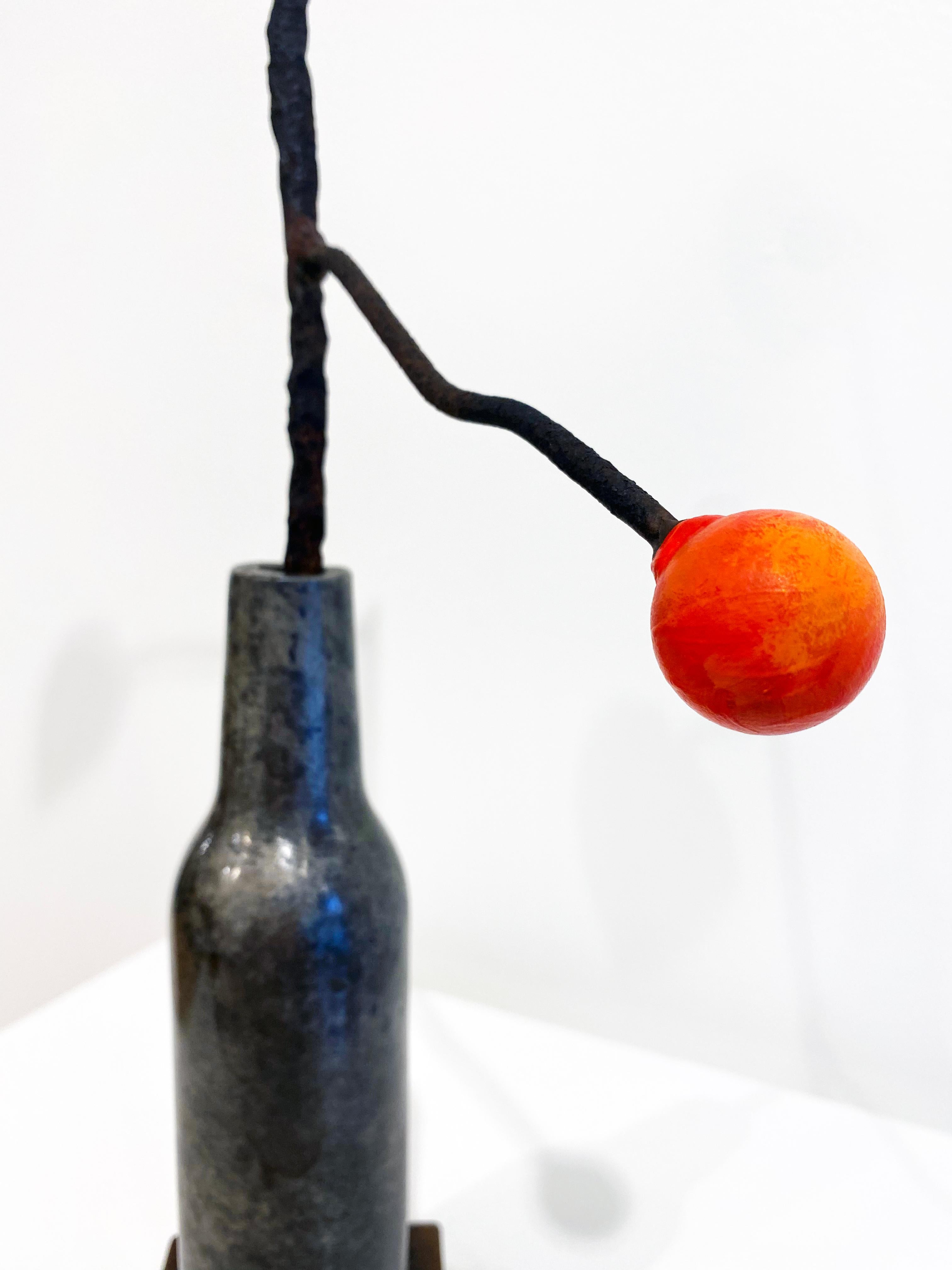 'Untitled 1' by David Kimball Anderson, 2021. Bronze, steel, and paint, 18 x 8 x 8 in. This sculpture features a rounded vase cast in bronze and finished in patinas of grey. It features a steel branch extending to  an orange bulb and green