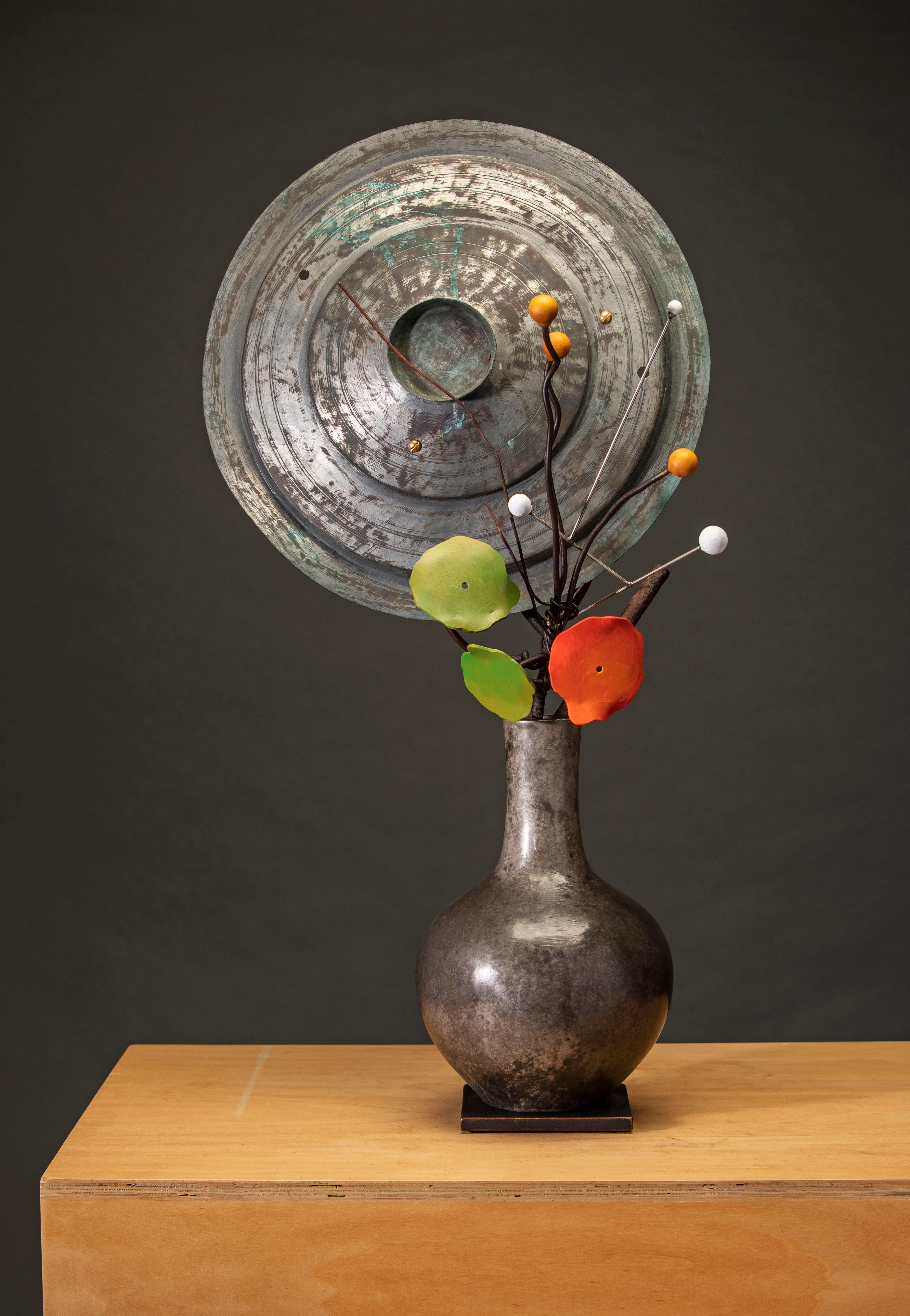 "Planètes, graines, capucines" par David Kimball Anderson, 2022. Bronze, acier, et peinture, 36 x 17 x 10 in. Cette sculpture présente un vase arrondi coulé en bronze et fini en patine grise. Il présente une série de branches en bronze et deux